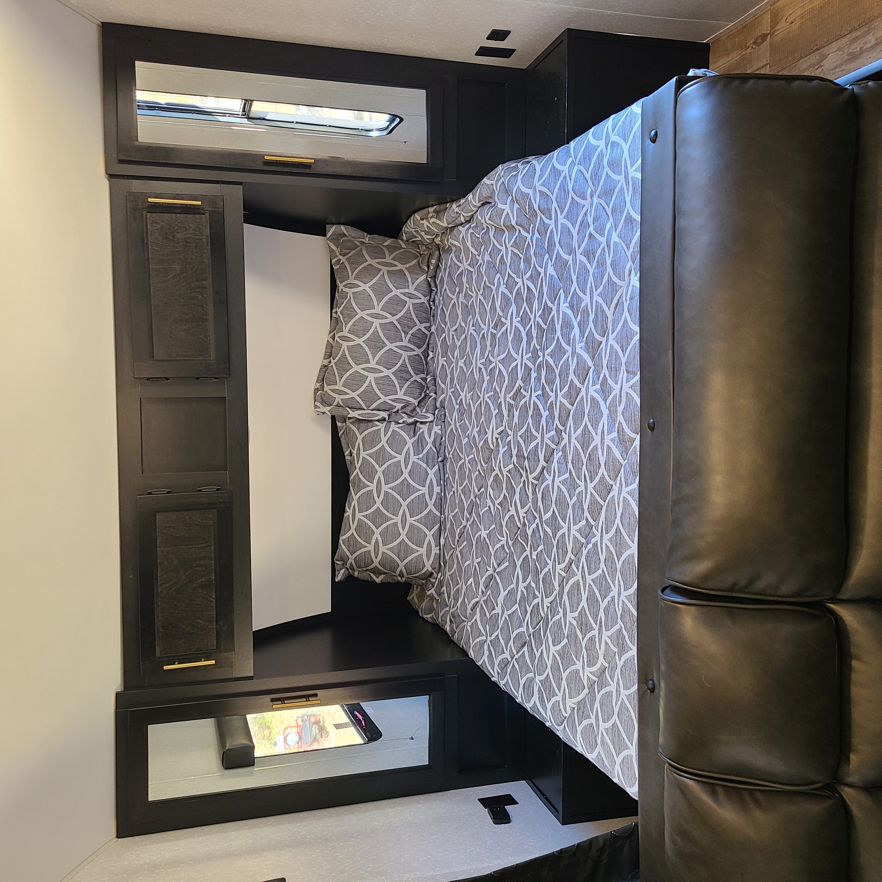 Inside an RV rental, a well-appointed bedroom features a bed with geometric grey bedding, dark storage cabinets, and a plush leather sofa.. Forest River Cherokee Grey Wolf Special Edition 2022