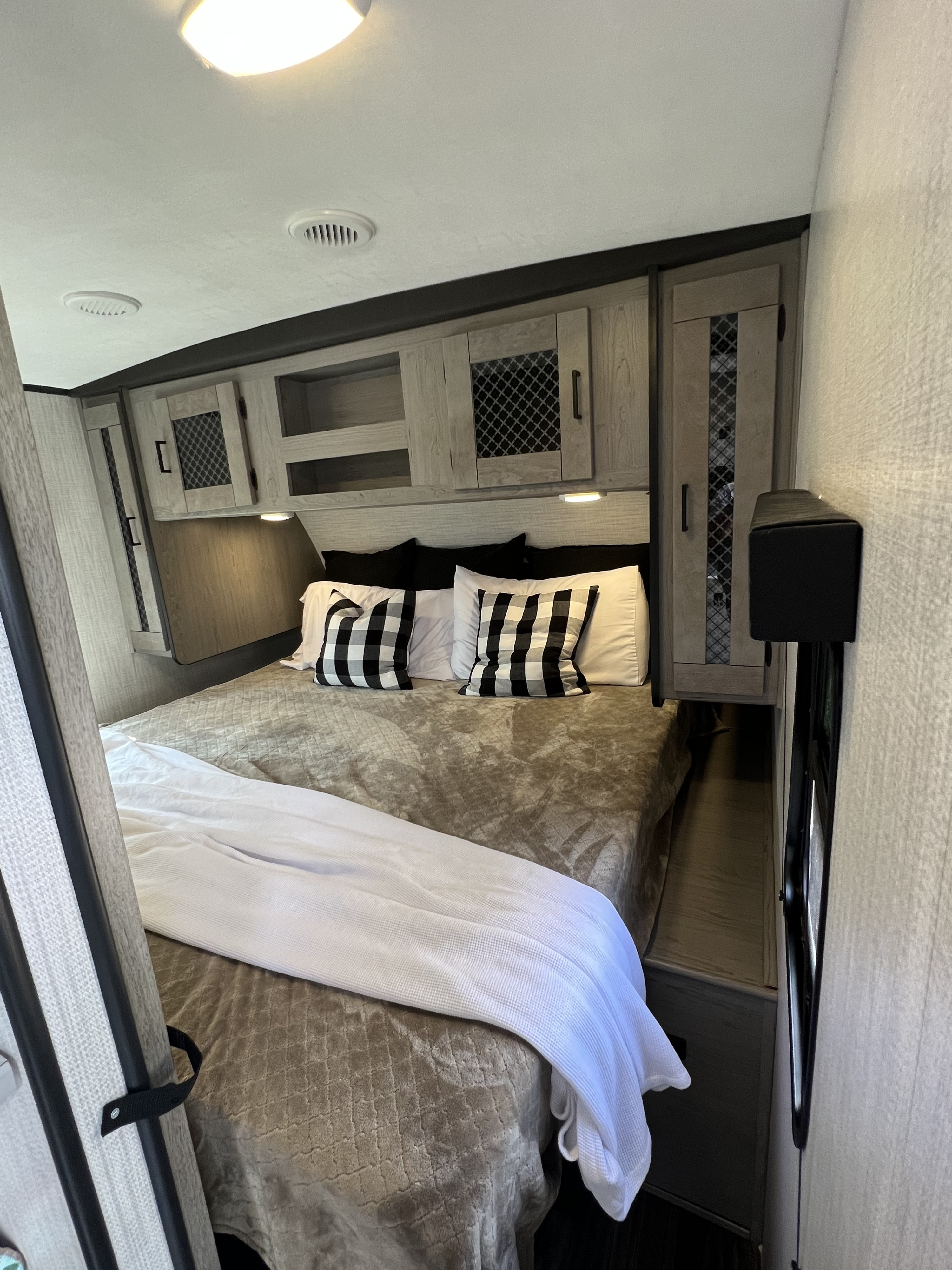 Cozy RV rental bedroom with a large bed, featuring white sheets, checkered pillows, and ample overhead storage for travel.. Heartland RVs Mallard 2021