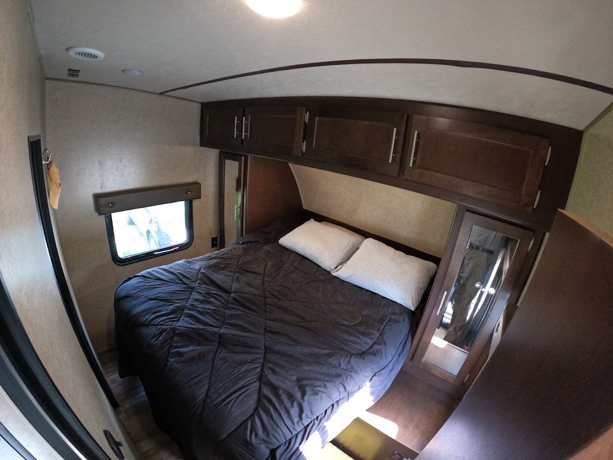Cozy RV rental bedroom with a comfy bed, overhead cabinets, and window. Ideal for compact living.. Forest River XLR Boost Toy Hauler 2018