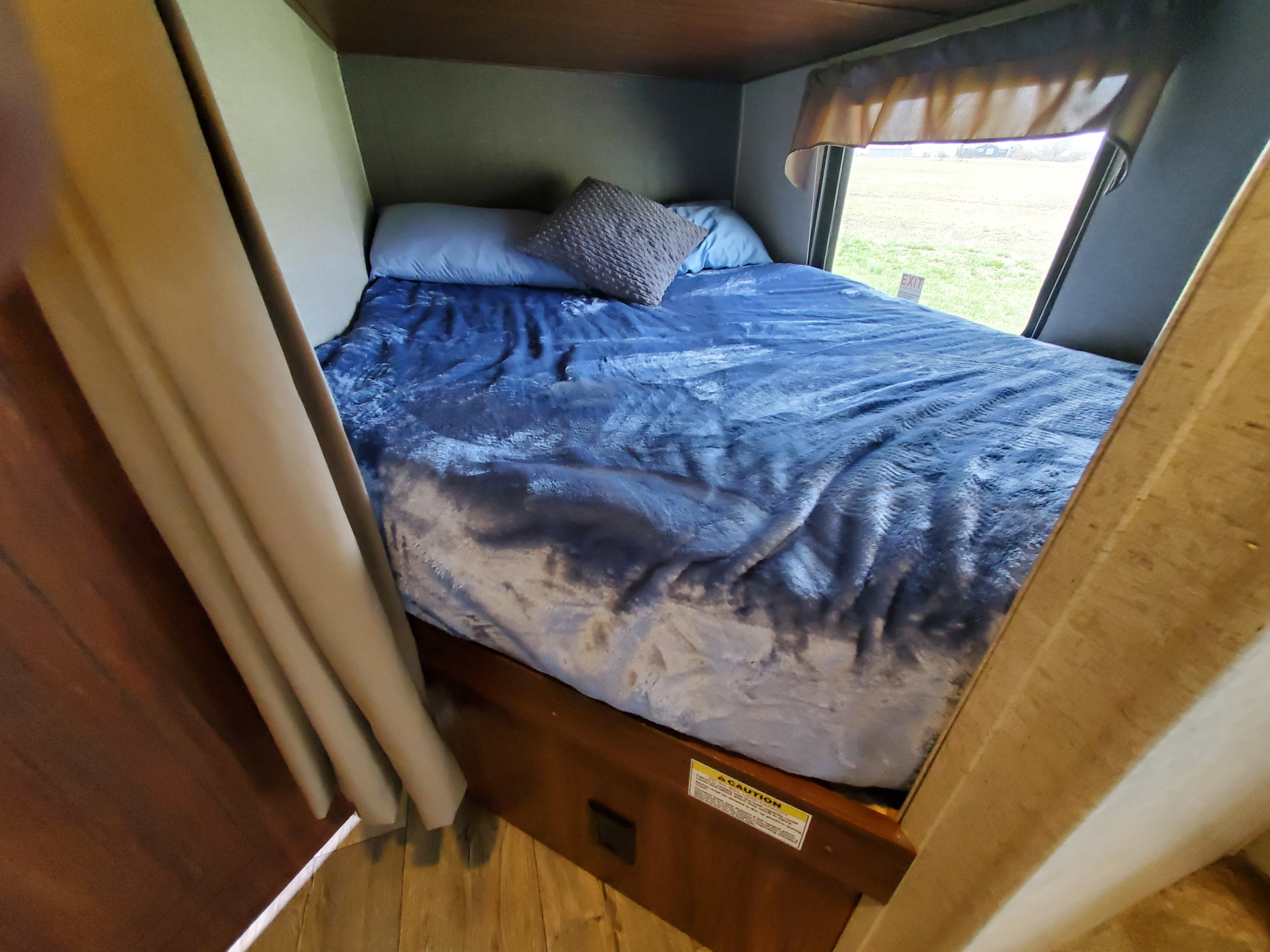 RV rental: A cozy bedroom with a blue blanket, pillows, and a window showing a field with an EXIT sign.. Heartland RVs Mallard 2017
