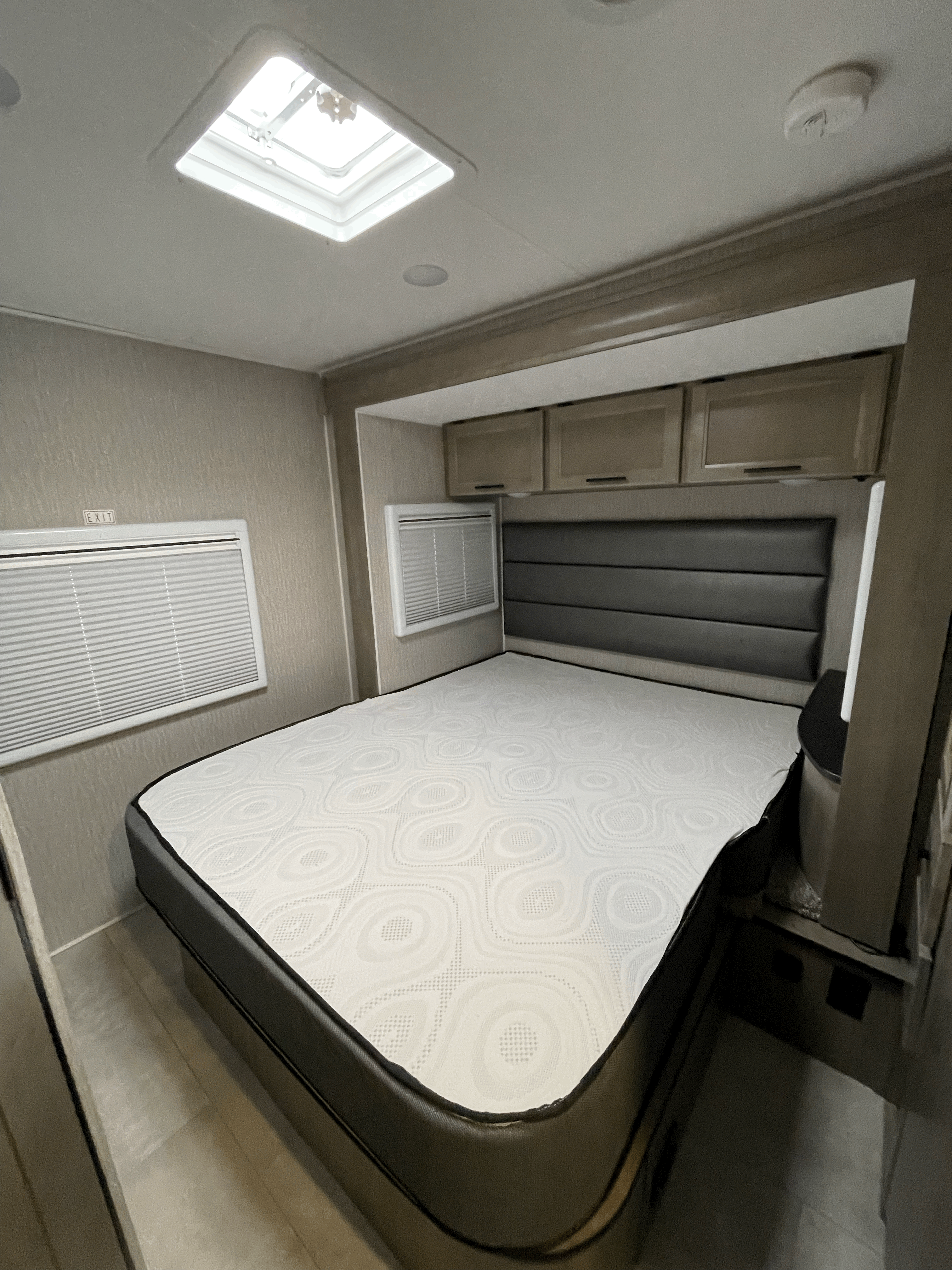 Experience comfort in this RV rental bedroom with a large bed, padded headboard, ample storage, and natural light from the skylight.. Coachmen Prism 2023