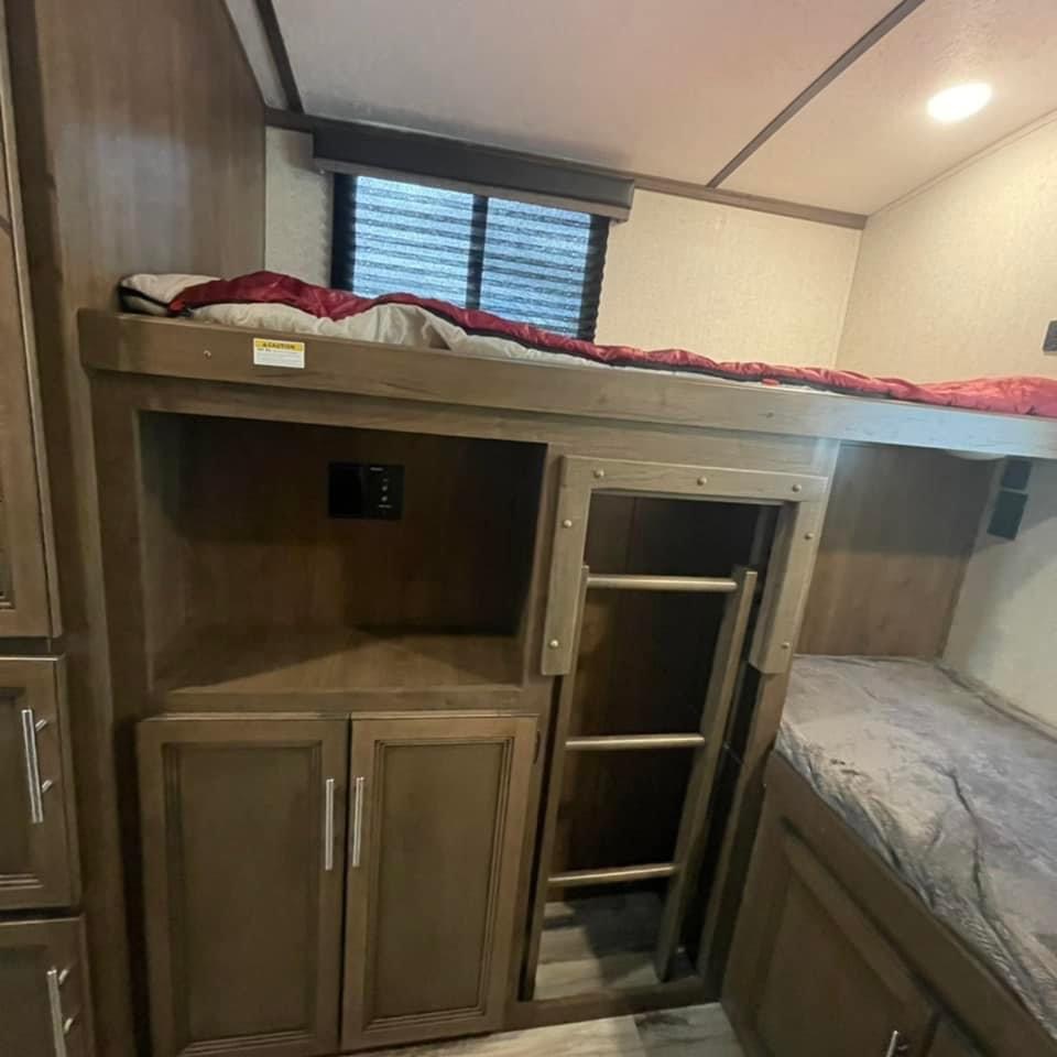 Spacious RV rental interior with comfortable bunk beds, built-in storage, and a ladder for access.. Keystone RV Cougar 2020