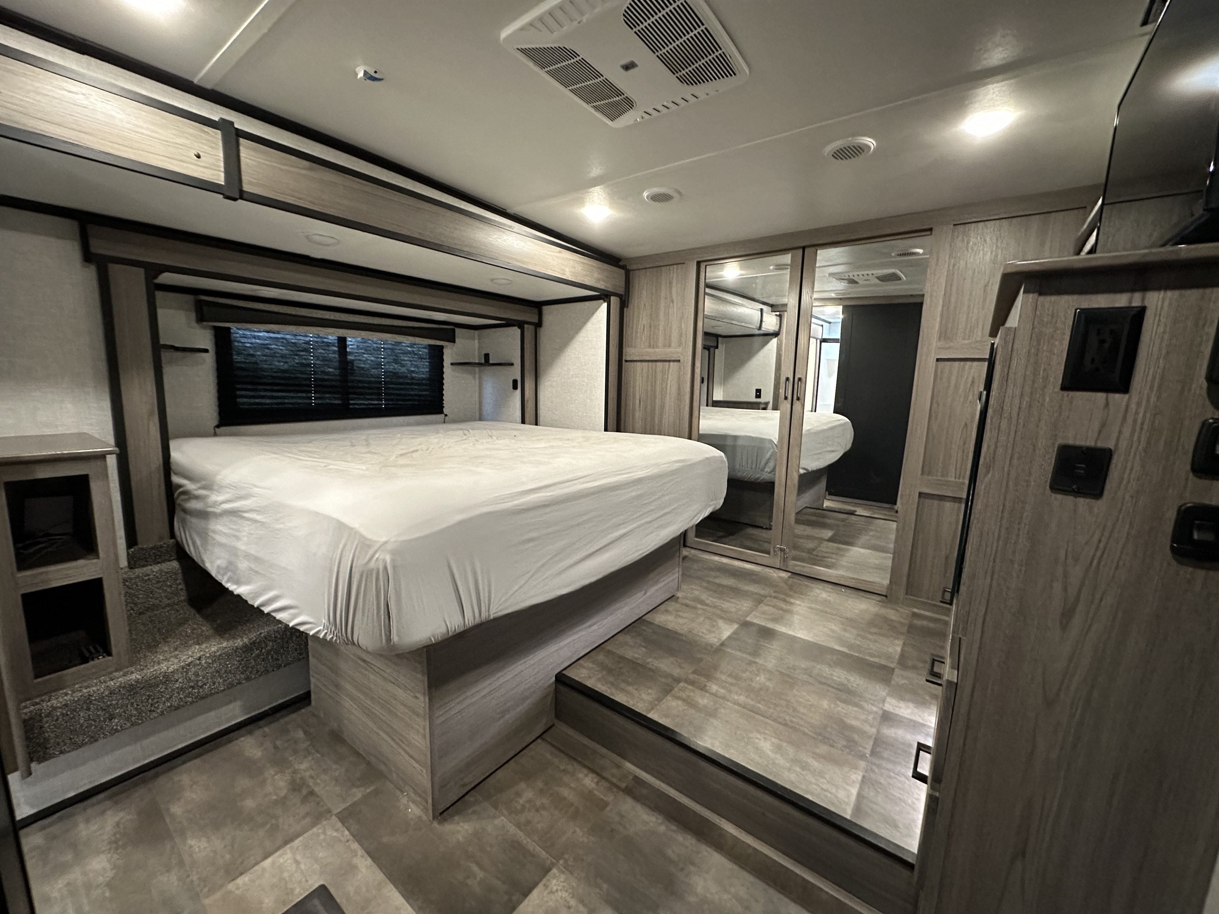 Spacious RV rental bedroom showcasing a large bed, stepped platform, and mirrored wardrobe for comfortable stays.. Crossroads RV Cameo 2022