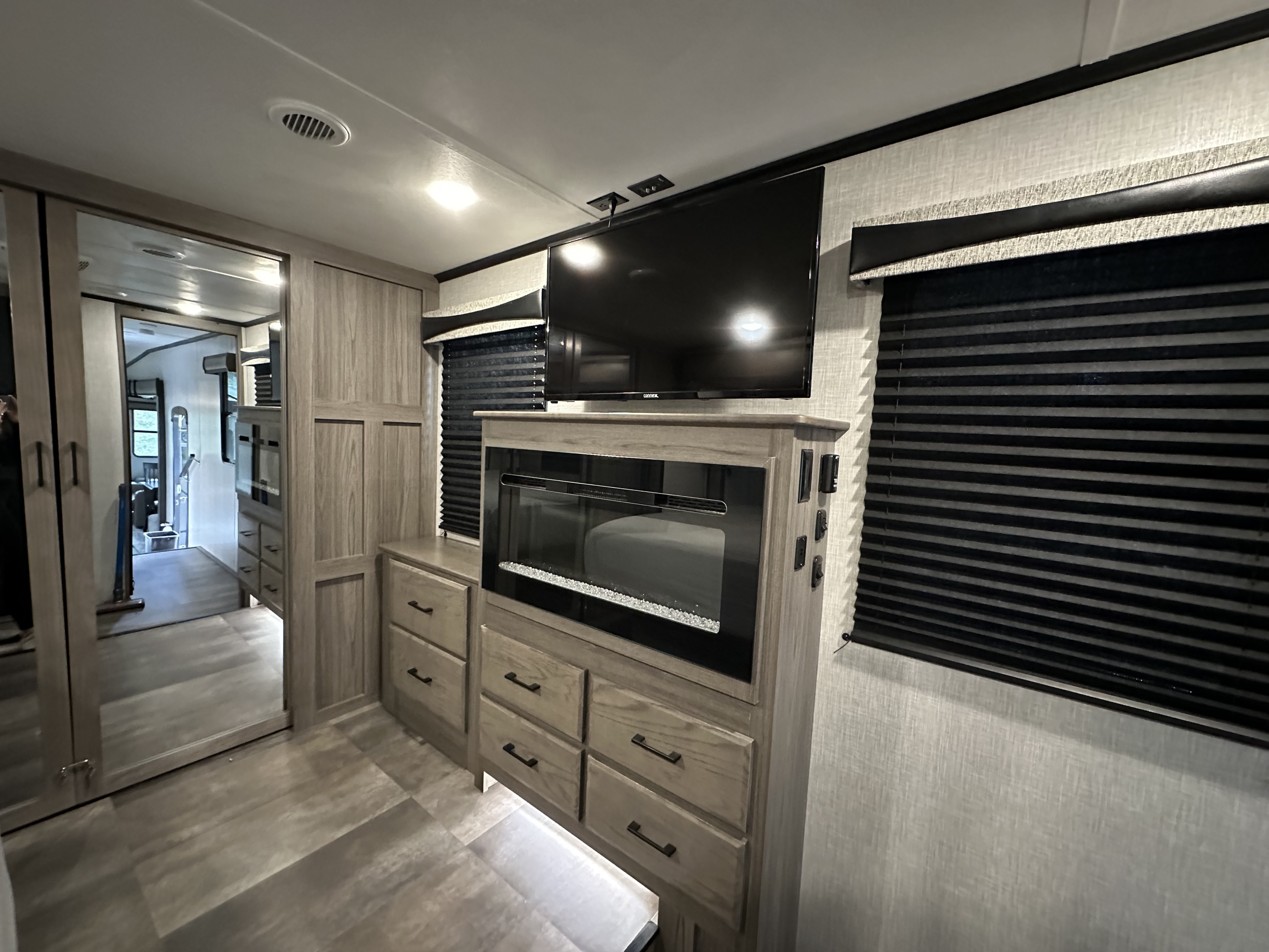 Modern RV rental interior showcasing a mounted TV, electric fireplace, and ample light wood-tone storage cabinetry in the main living area.. Crossroads RV Cameo 2022