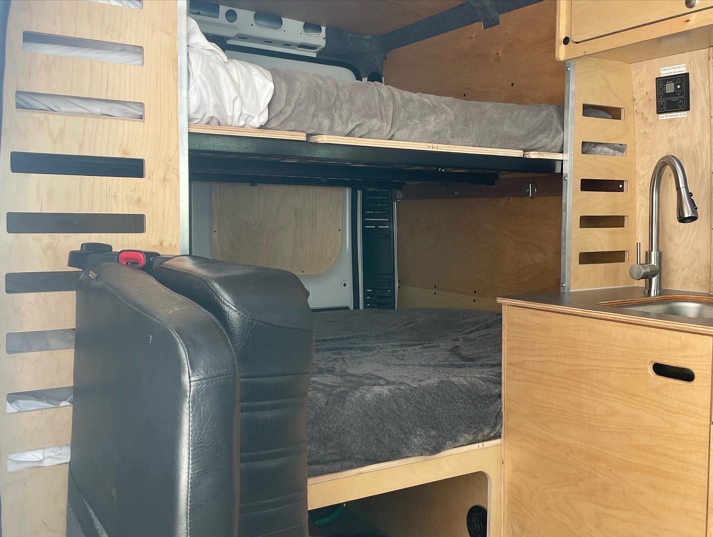 RV rental interior with wooden bunk beds, a compact kitchenette with sink, and black upholstered seating.. RAM ProMaster 2023