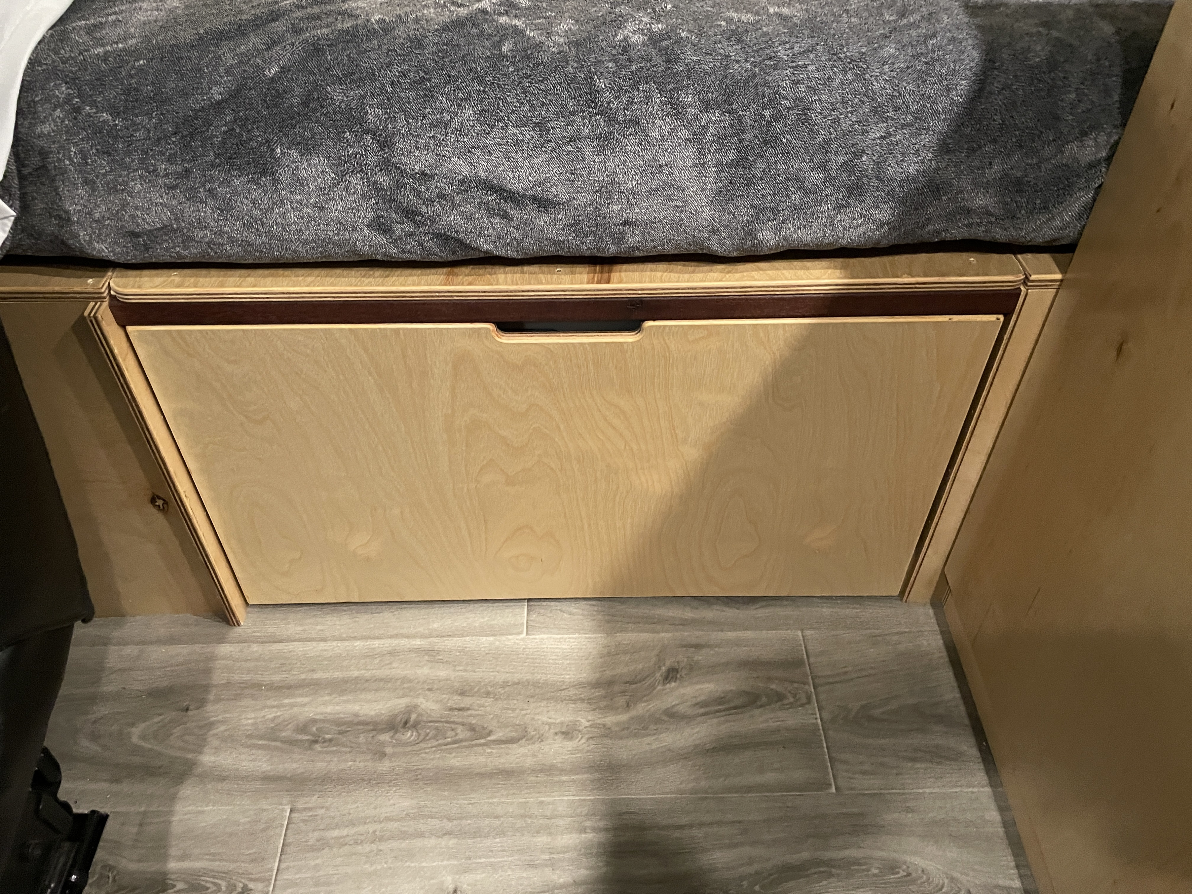 RV rental: Under-bed storage with a light wood drawer, dark trim, and a cutout handle. Gray bed and laminate floor visible.. RAM ProMaster 2023