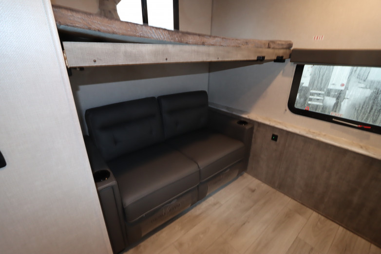 RV rental interior: A cozy bunk bed over a two-seater couch with cup holders, next to a window. Wood laminate flooring.. Forest River Surveyor 2023