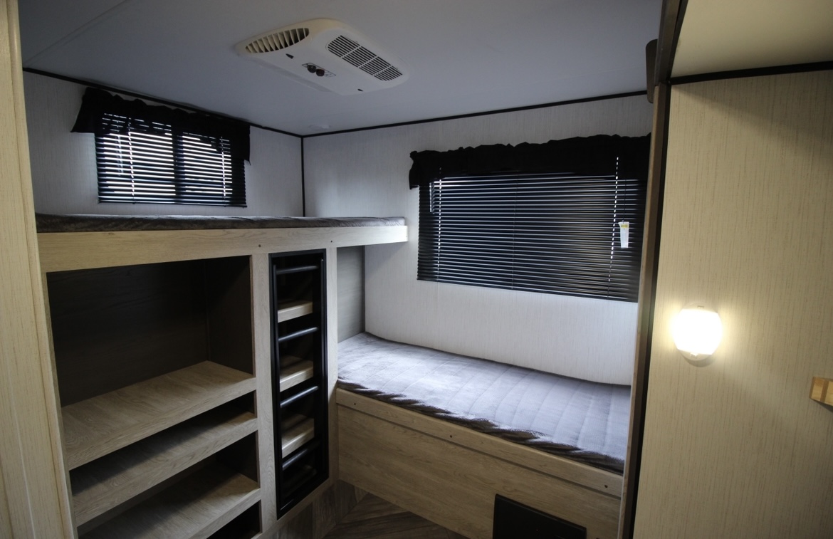 RV rental interior showcasing a cozy bunk area with two beds, shelving storage, and windows, ideal for family travel.. Heartland RVs Prowler 2022