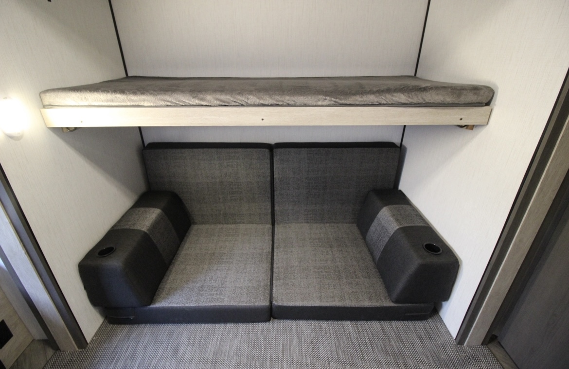Cozy RV rental interior featuring a bunk bed over a two-section sofa with armrests & cup holders, ideal for compact living.. Heartland RVs Prowler 2022