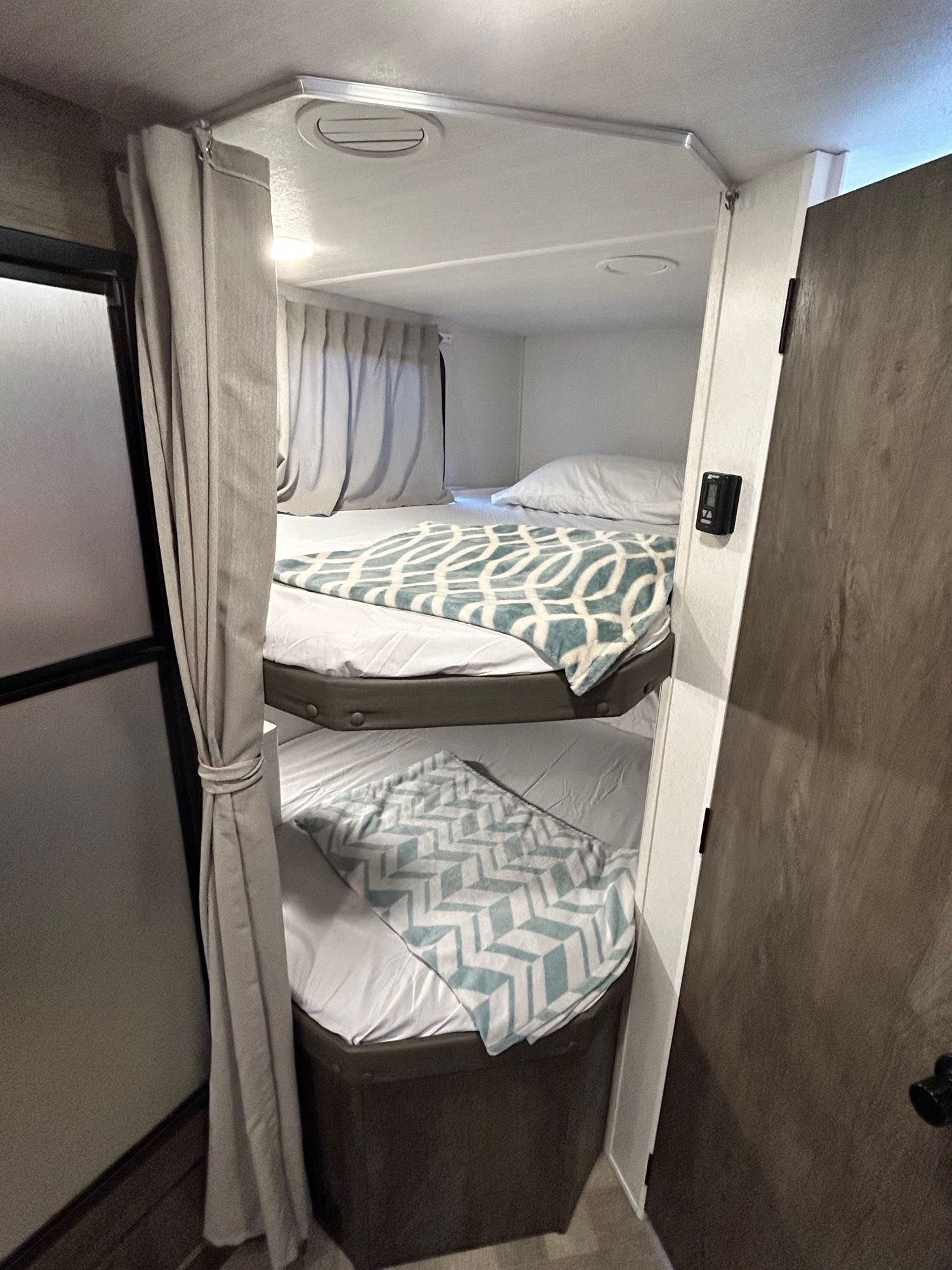 Cozy bunk beds in an RV rental, complete with patterned blankets and privacy curtains, ideal for family travel.. Forest River Wildwood X-Lite 2021