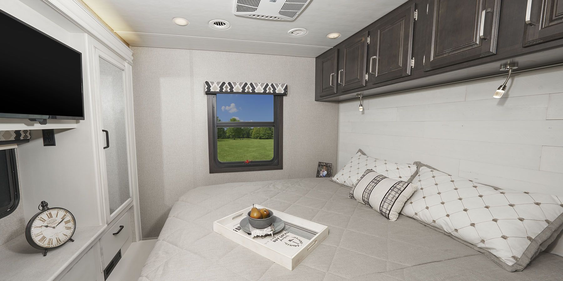Cozy RV rental bedroom featuring a spacious bed, window with nature view, TV, and overhead storage.. Jayco Precept 2020