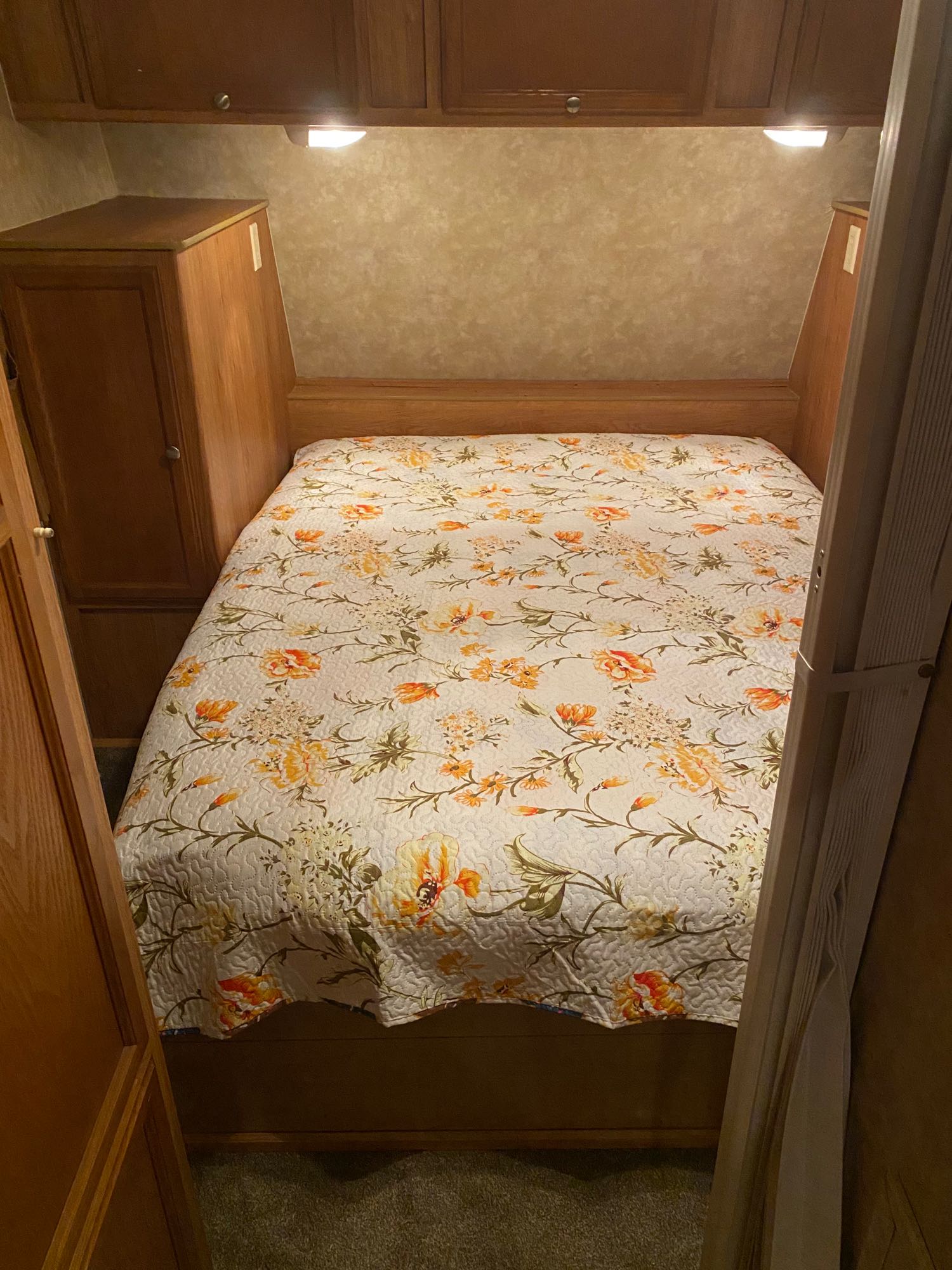 Cozy RV rental bedroom with a floral bedspread, built-in storage, and overhead lights, offering a compact sleeping area.. Jayco Jay Feather 2007