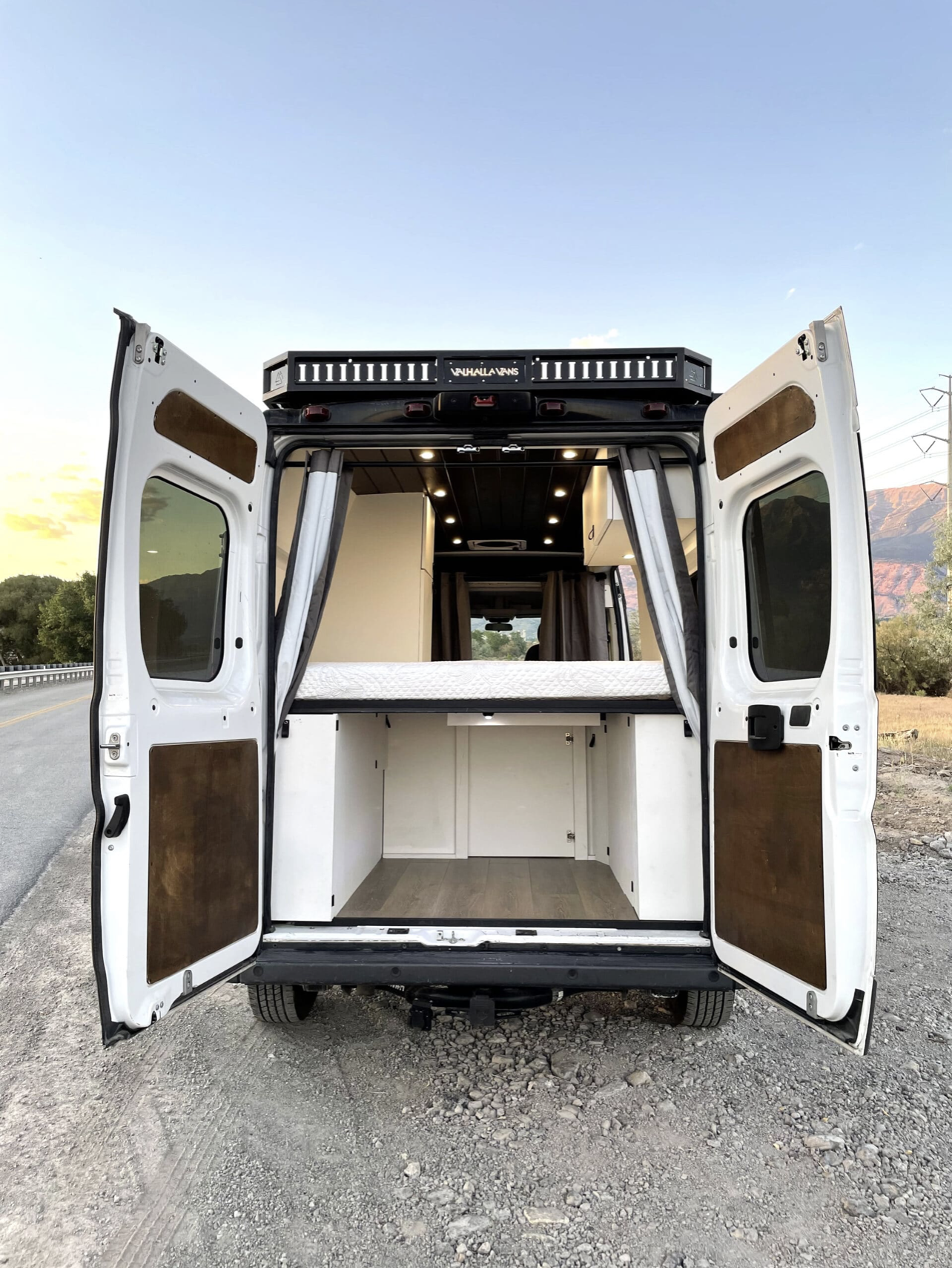 Inside a white custom camper van conversion, perfect for your next rv rental adventure. Features a raised bed and under-bed storage.. Dodge Sprinter Van 2016
