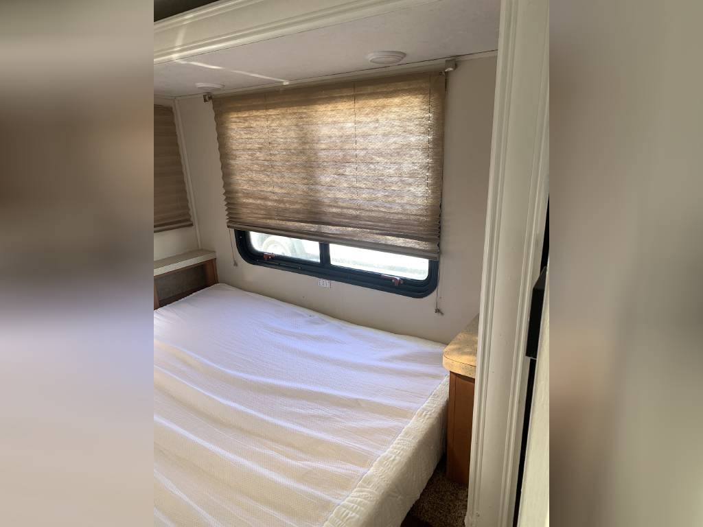 RV rental bedroom: Compact space with a white-covered bed, window with light brown blinds, and small cabinet. Ideal for travel.. Forest River Sunseeker 2015