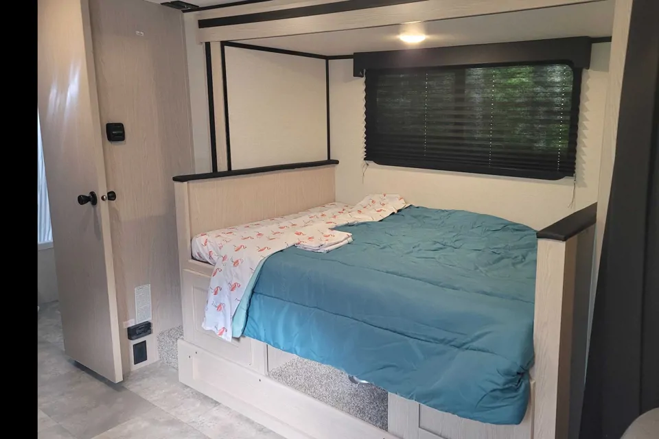 This inviting RV rental bedroom features a comfy bed with teal comforter, light wood furniture, and a window.. Coachman Apex Nano 208BHS 2022