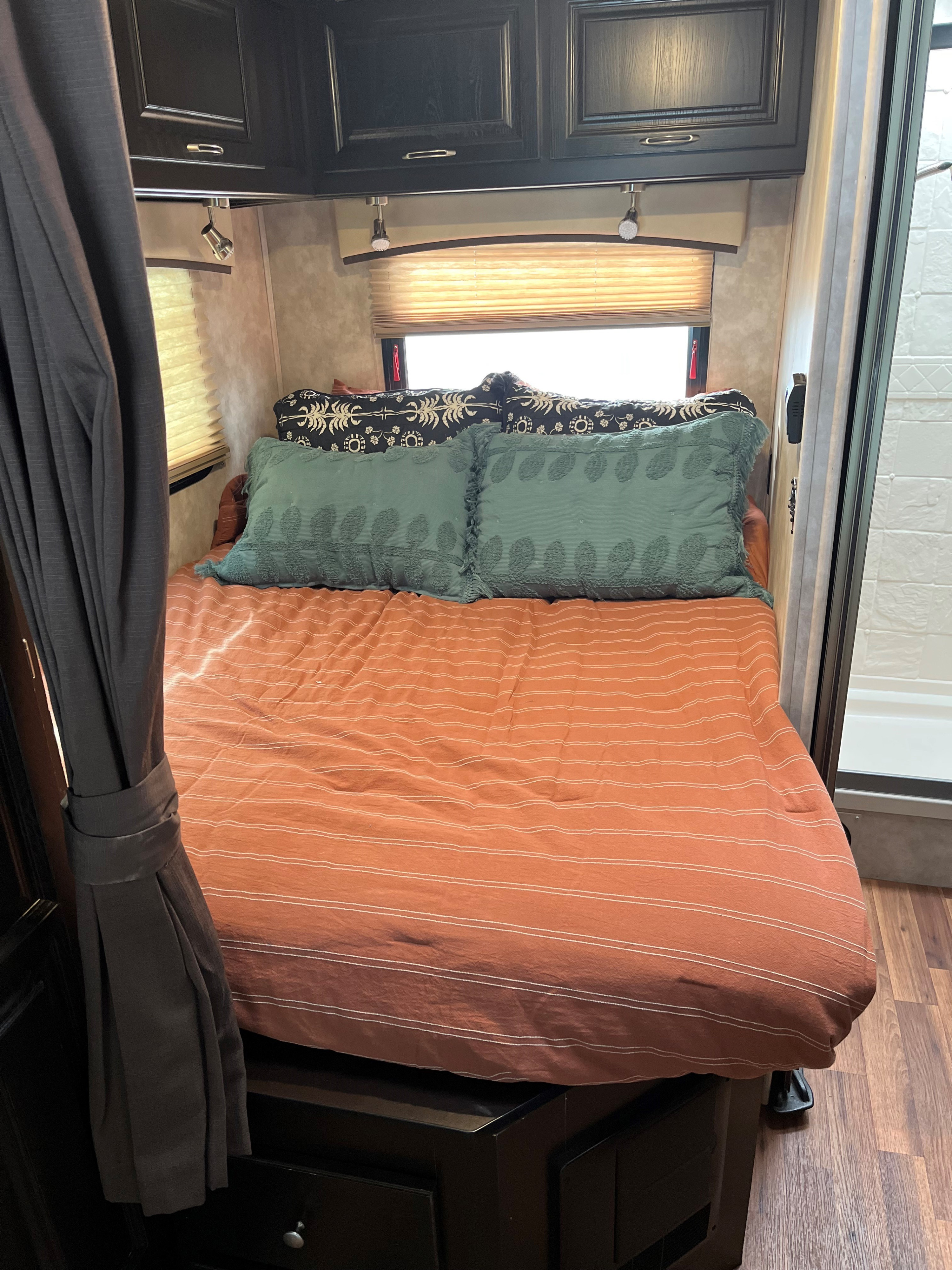 Compact RV rental bedroom with a warm orange bed, dark cabinets, window blinds, and adjacent shower.. Nexus RV Phantom 2016