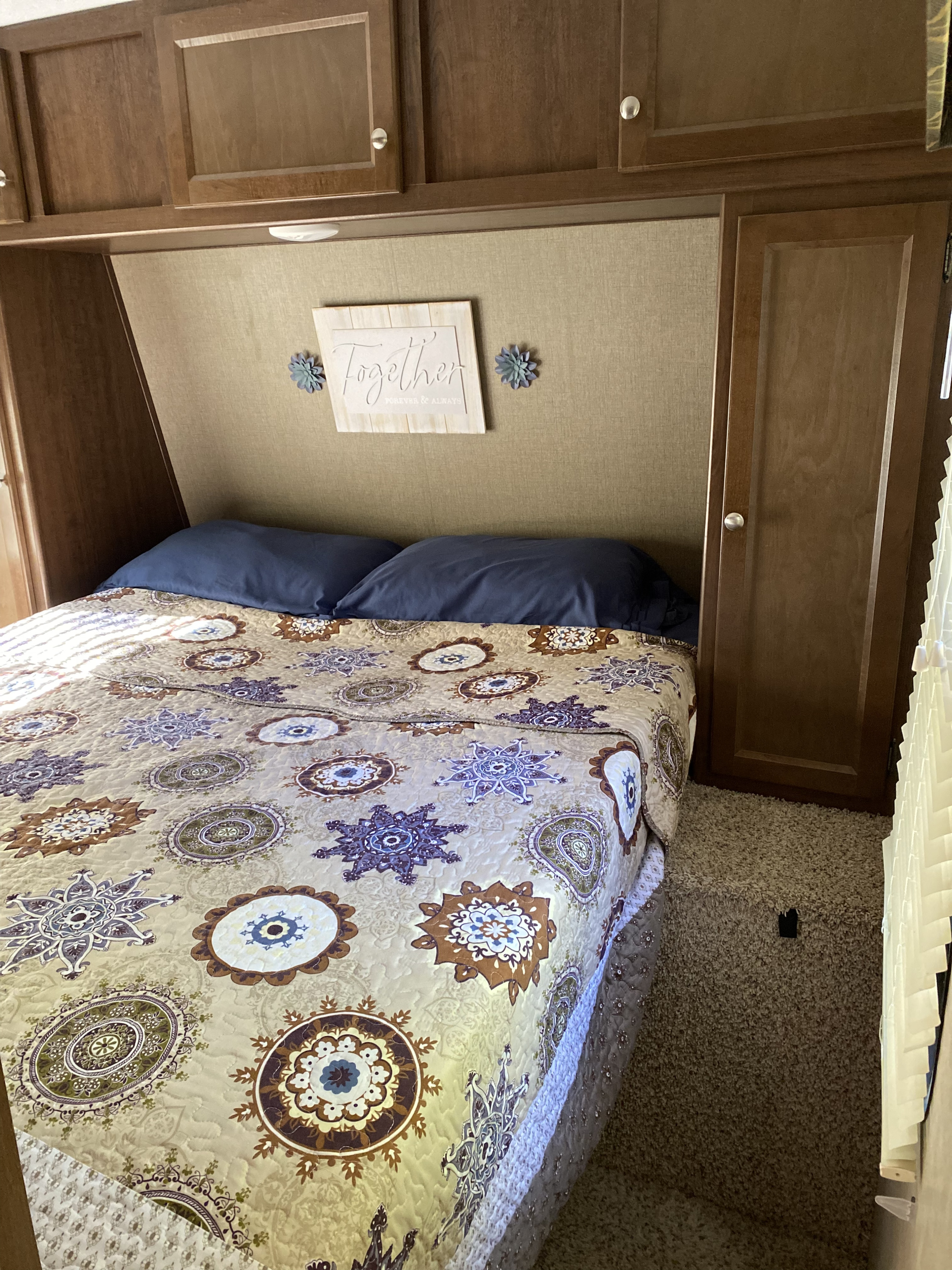 Cozy RV rental bedroom: bed with patterned quilt, blue pillows, overhead cabinets, and a 'Together' sign on the wall.. Keystone RV Hideout 2016