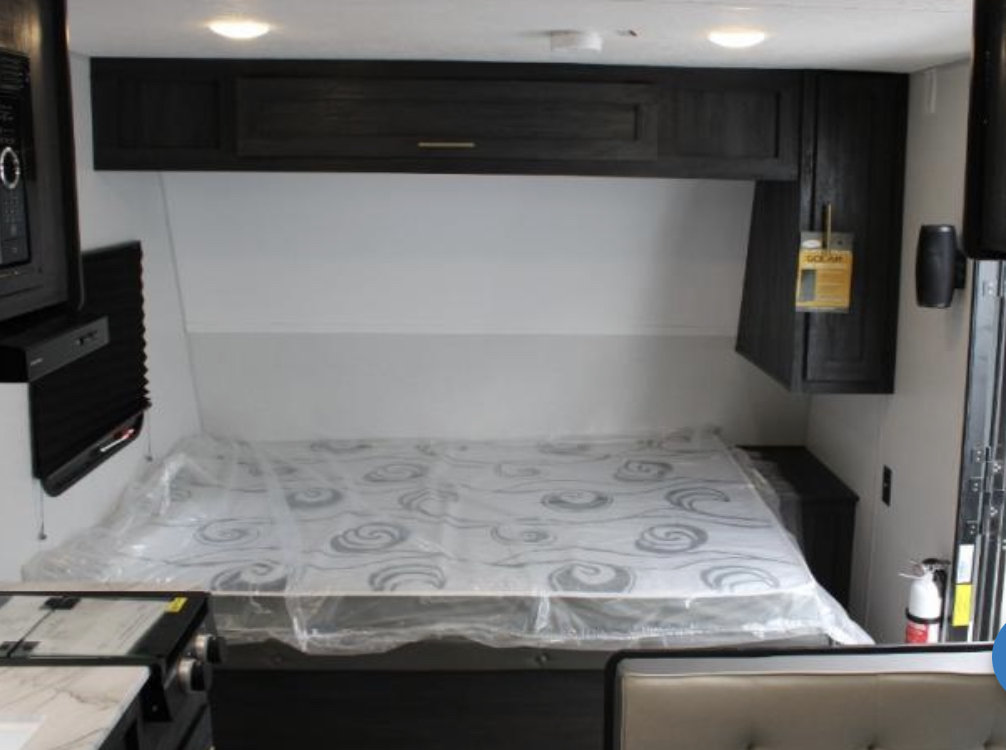 Inside an RV rental: view of the bedroom with a plastic-covered mattress, overhead storage, and entertainment area.. Forest River Ozark 1650BHKX 2022