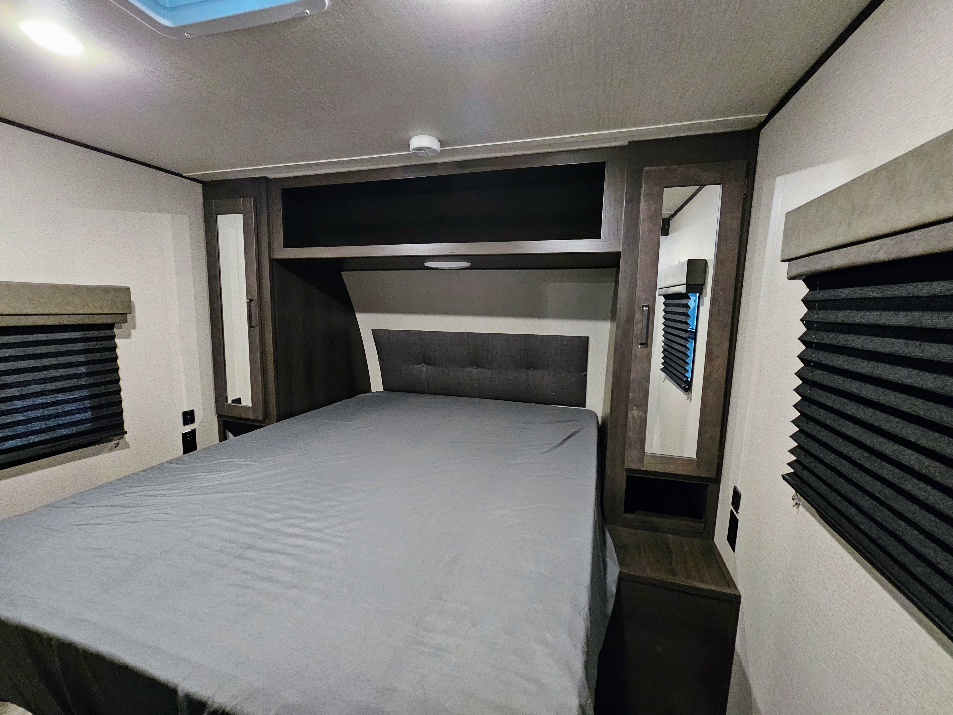 A comfortable RV rental bedroom featuring a full bed, built-in storage, side cabinets, and blackout blinds for privacy.. Grand Design Transcend 2022