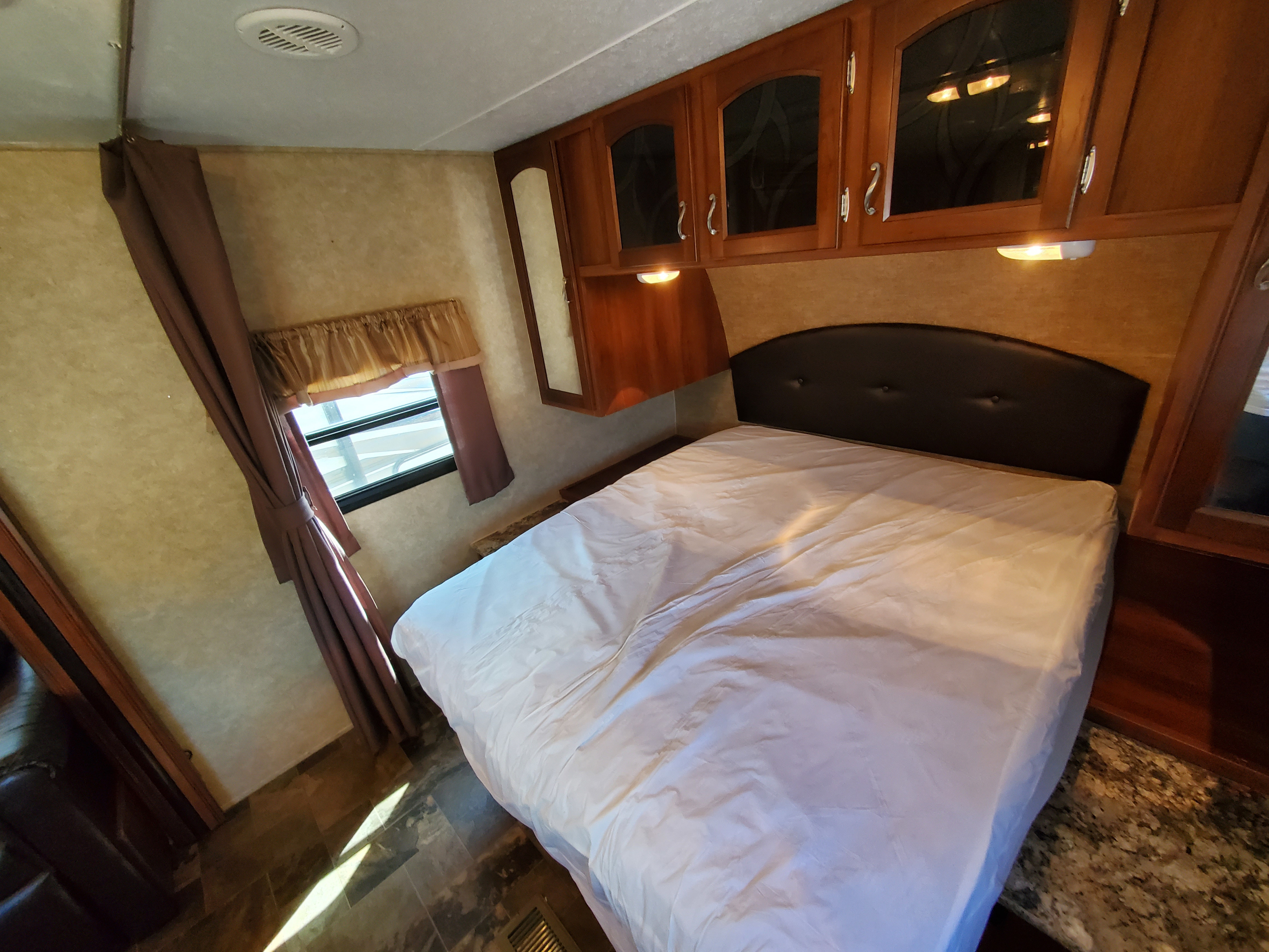 Cozy RV rental bedroom featuring a comfortable bed, overhead cabinets, and a window for natural light.. Prime Time Tracer 2015