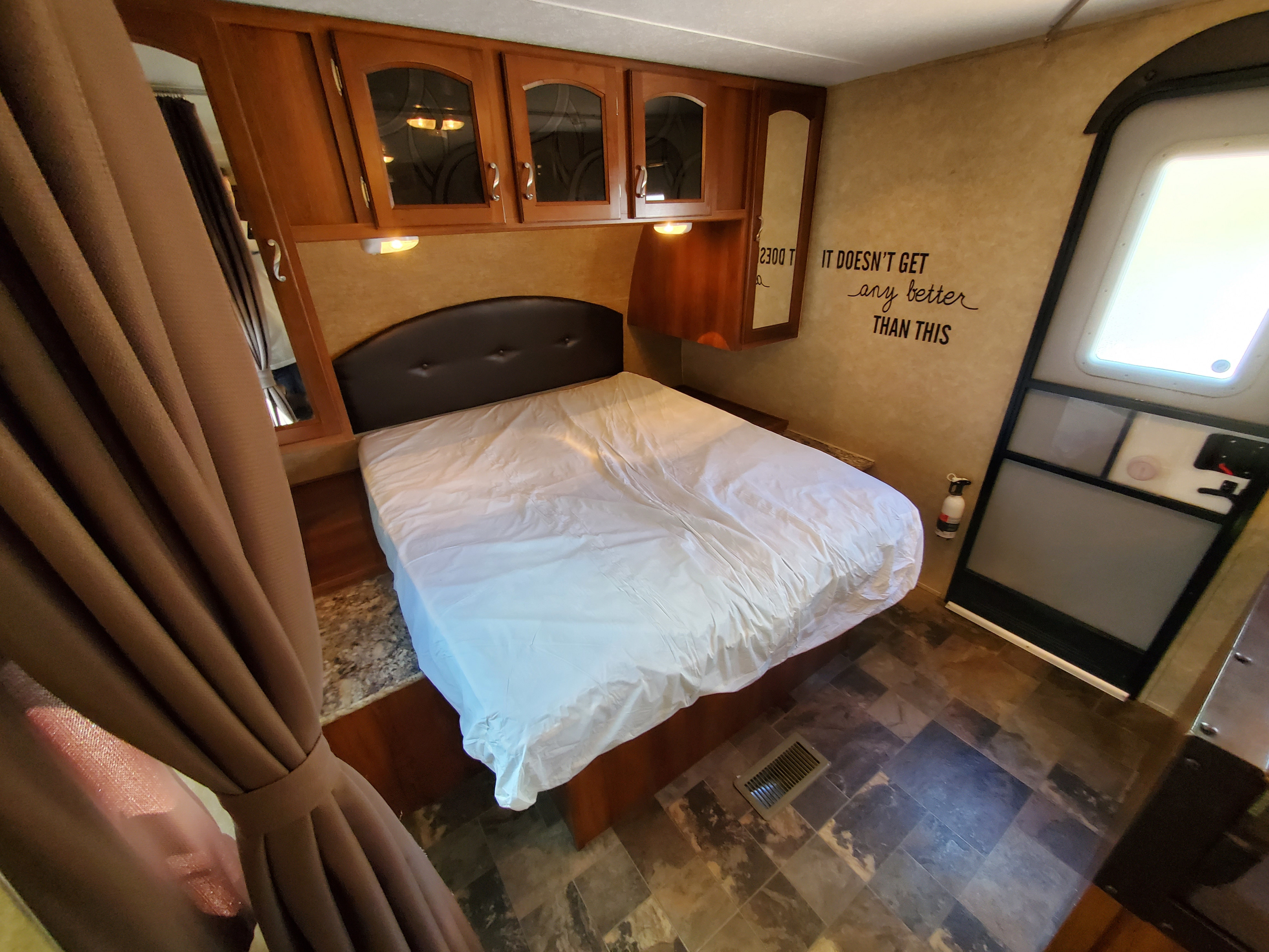 RV rental bedroom: cozy bed, wood cabinets, soft curtains, and a positive wall decal for a comfortable stay.. Prime Time Tracer 2015