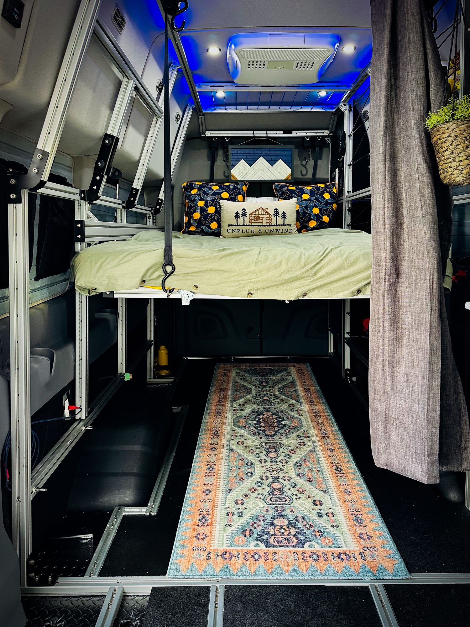 Modern rv rental interior: suspended bed on aluminum frame, colorful rug, and ample space below for travel.. Vandoit DO 2019