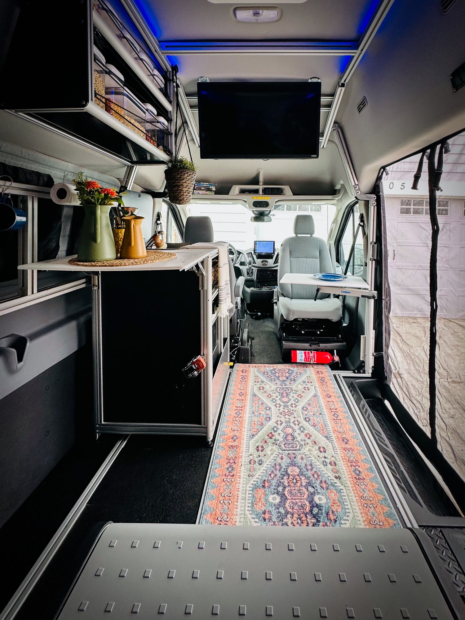 Explore a modern RV rental interior: functional kitchenette, swivel seat with table, smart overhead storage, and a colorful rug.. Vandoit DO 2019