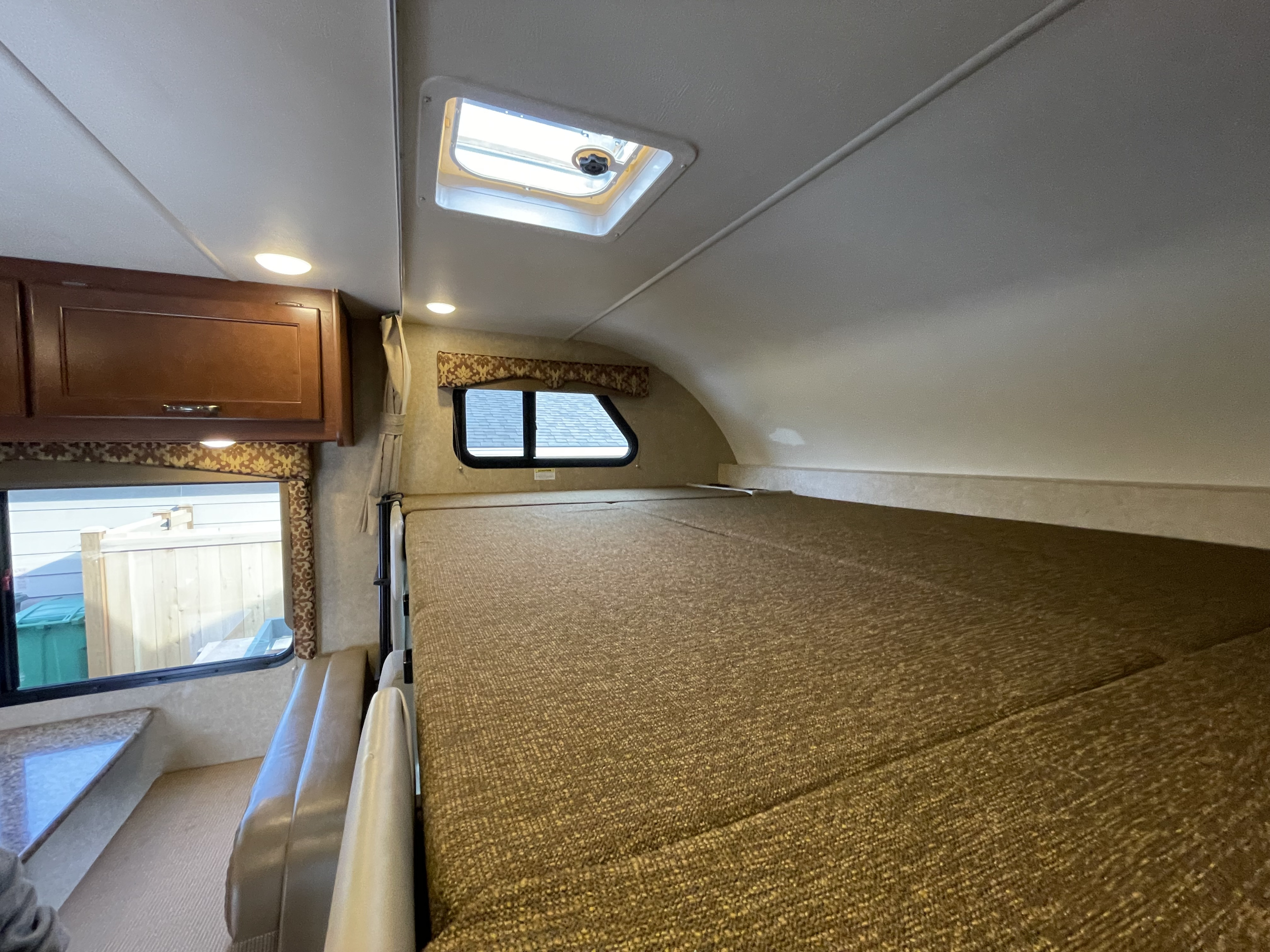 Inside an RV rental: a large overhead bunk bed, with a ceiling skylight and side window, offering a view outside.. Thor Freedom Elite 2017