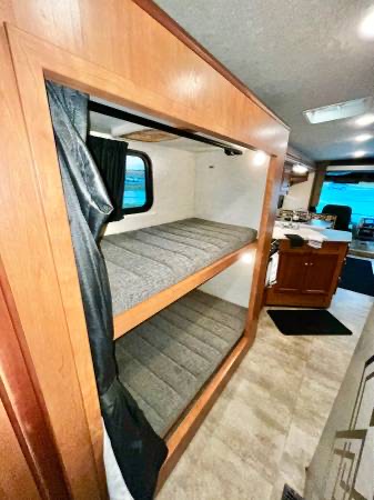 Bunk beds in an RV rental, featuring grey mattresses, privacy curtains, and individual lighting for a cozy sleep.. Winnebago Sunstar 2016