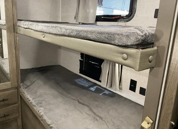 RV rental bunk beds with soft gray bedding, a window with blinds, and power outlets, offering comfortable sleeping.. Forest River Wildwood X-Lite 2020