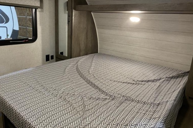 Spacious RV rental bedroom with a comfortable bed, stylish grey and white patterned sheets, a window, and an illuminated headboard.. Forest River Wildwood X-Lite 2020
