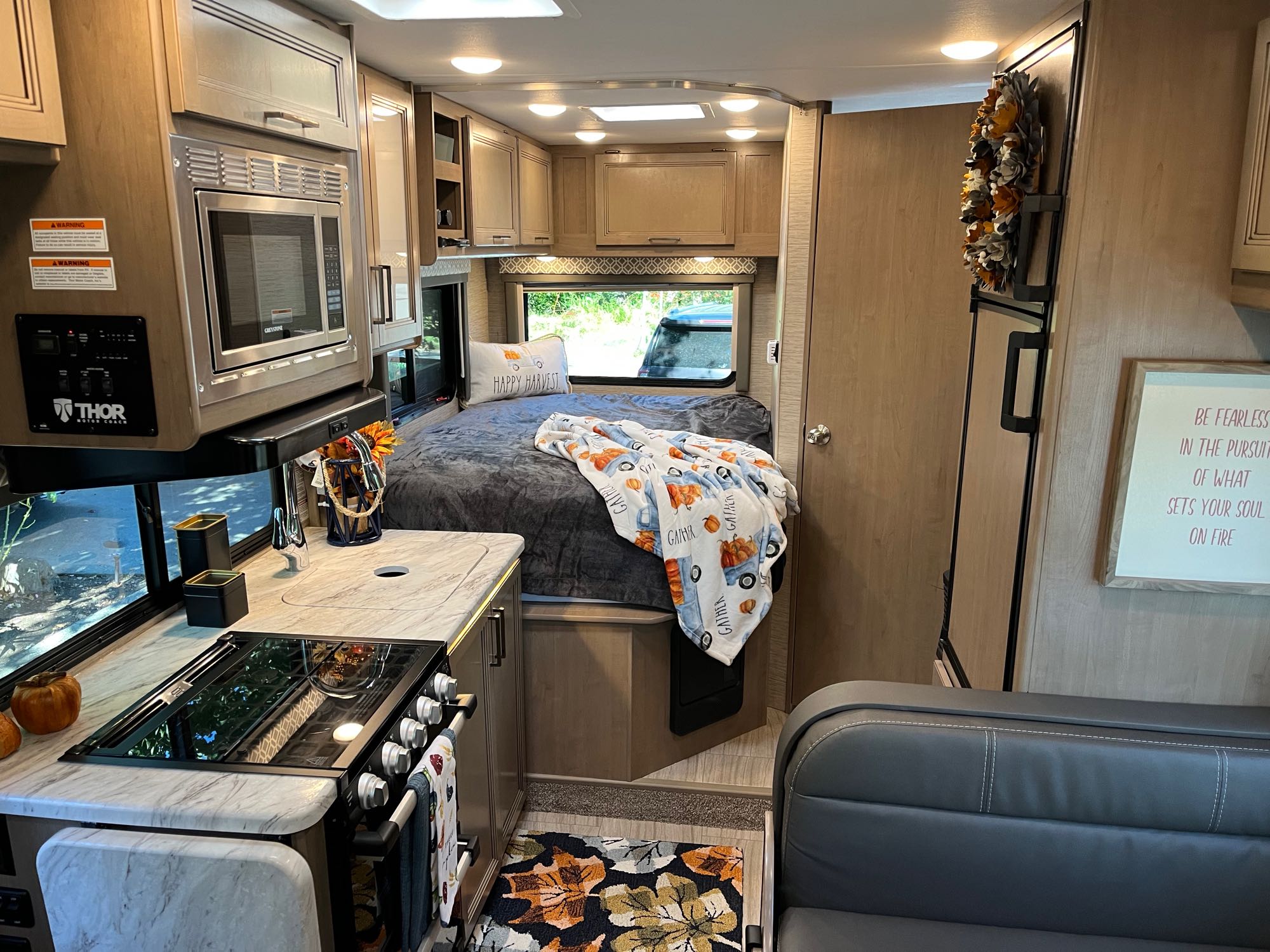A welcoming RV rental interior, showcasing a well-equipped kitchen, plush bed, and autumn-themed accents for a cozy journey.. Thor Motor Coach Other 2022