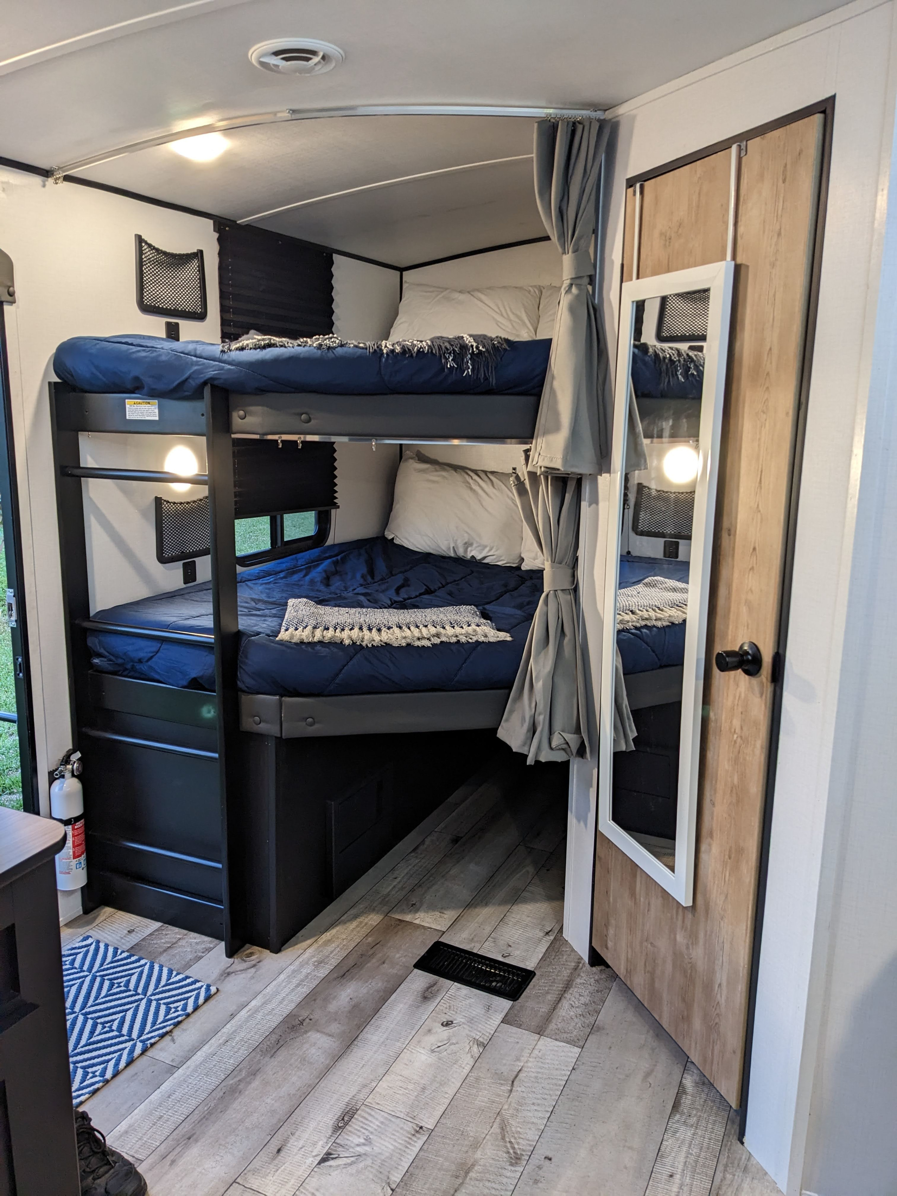 Cozy RV rental bunk bed area with navy blue bedding, individual reading light, privacy curtains, and wood-look floor.. Keystone RV Springdale 2022
