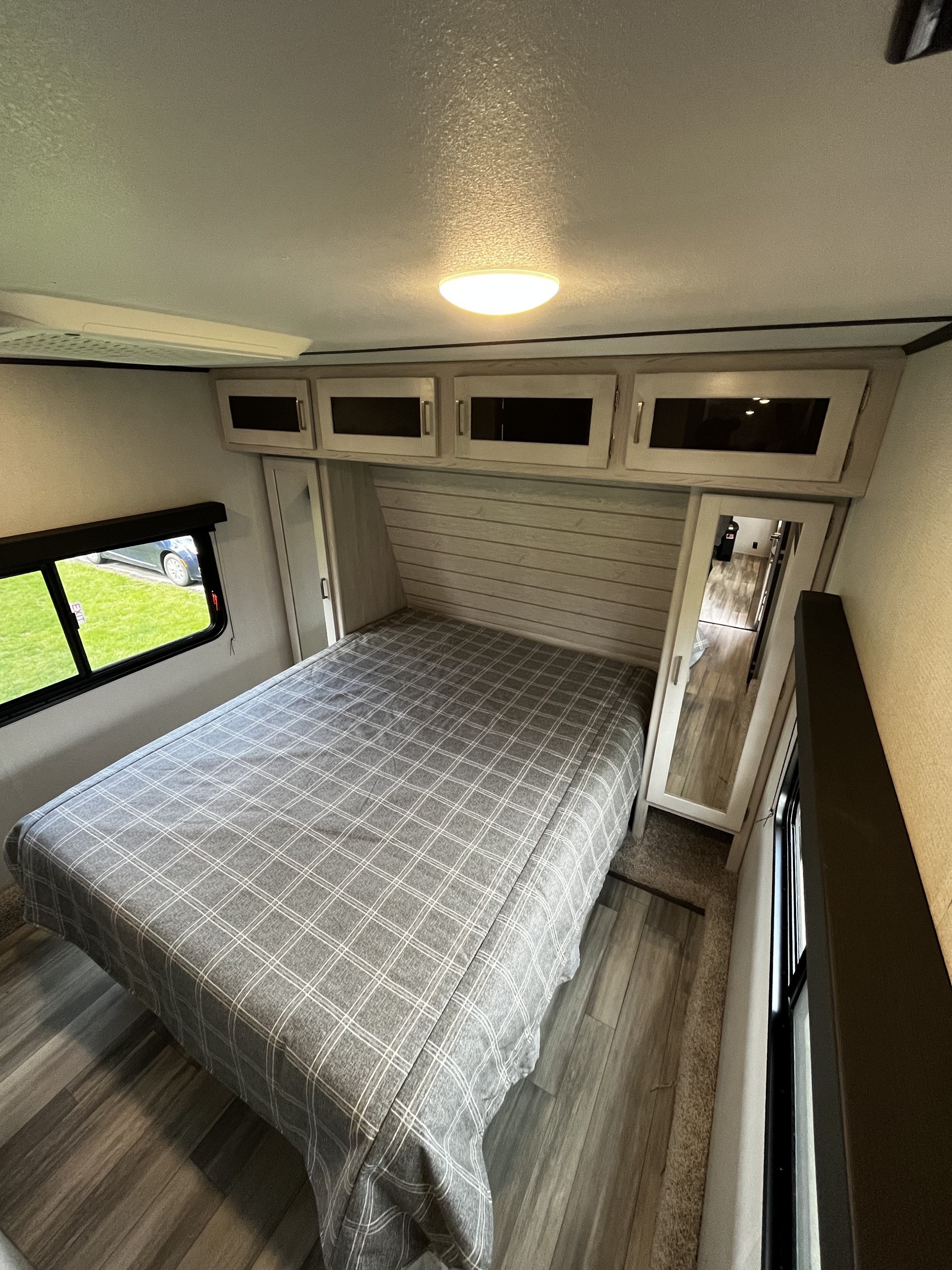 Inside a modern RV rental bedroom: cozy plaid bed, ample overhead storage, and window views.. Keystone Sprinter 2023