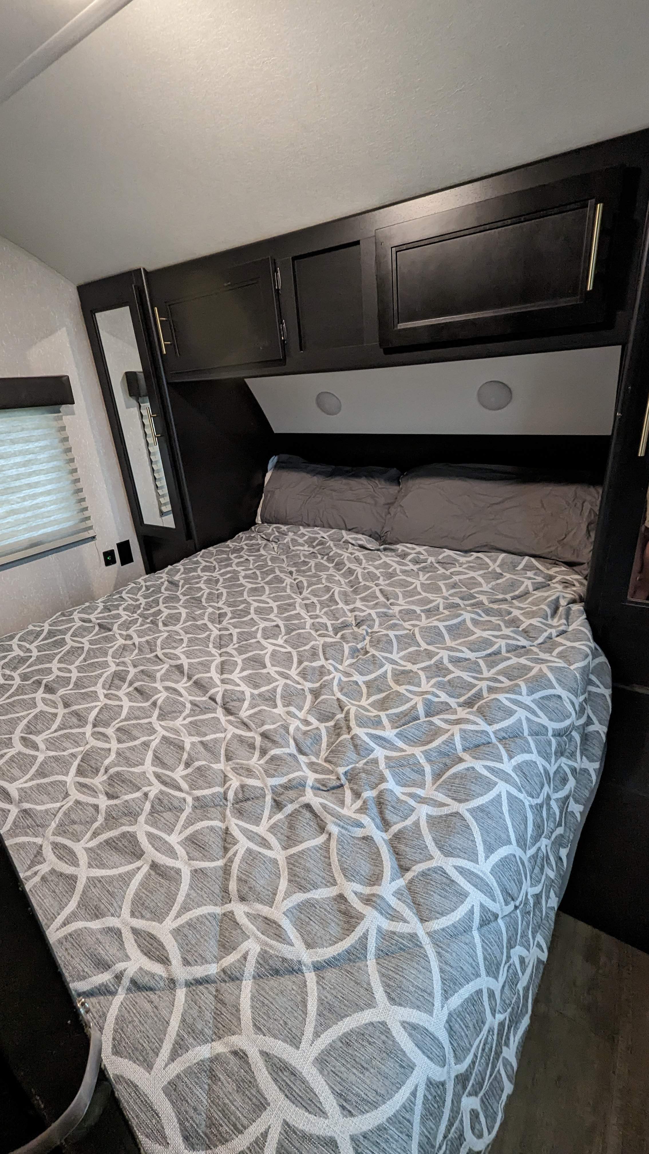 Cozy RV rental bedroom featuring a bed with a grey geometric comforter, dark cabinets, and built-in headboard lights.. Forest River Cherokee Grey Wolf Black Label 2021