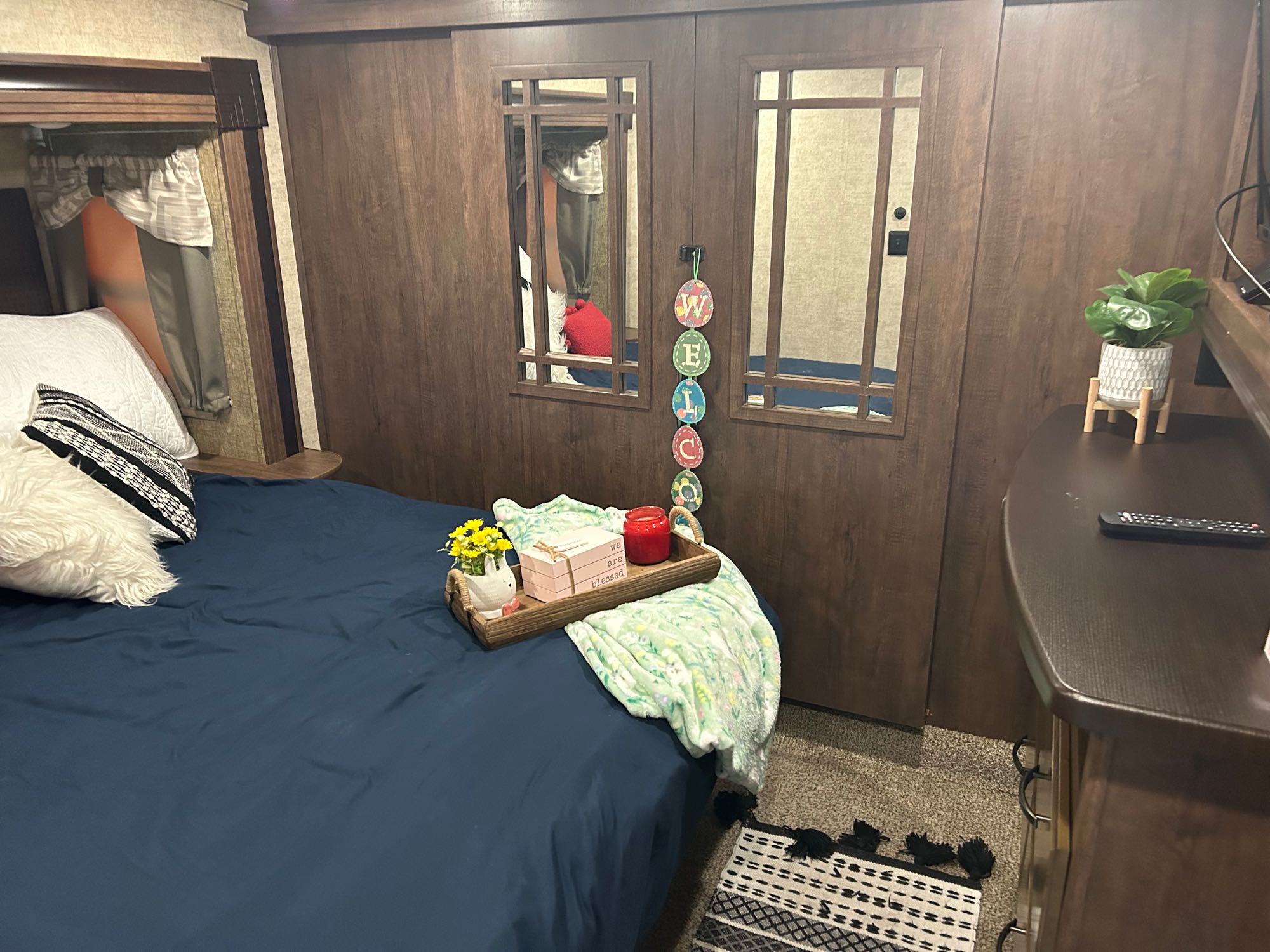 Inviting RV rental bedroom with blue bedding, decorative tray, mirrored doors, and a plant on the dresser.. Forest River Sandpiper 2018