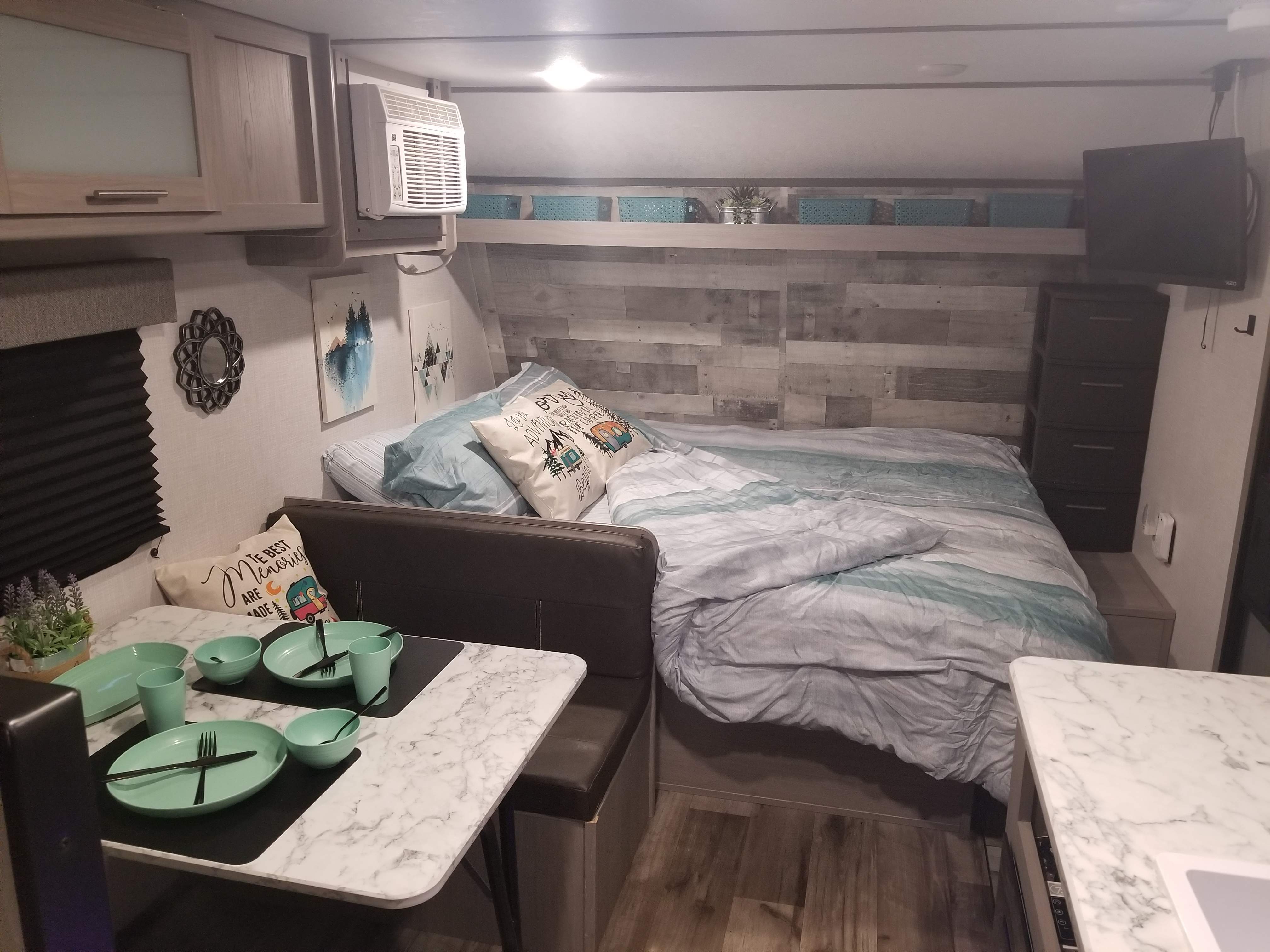Experience comfort in this RV rental! Features include a cozy bed, a dining area with mint green place settings, and ample storage.. Coleman Lantern 17B 2023