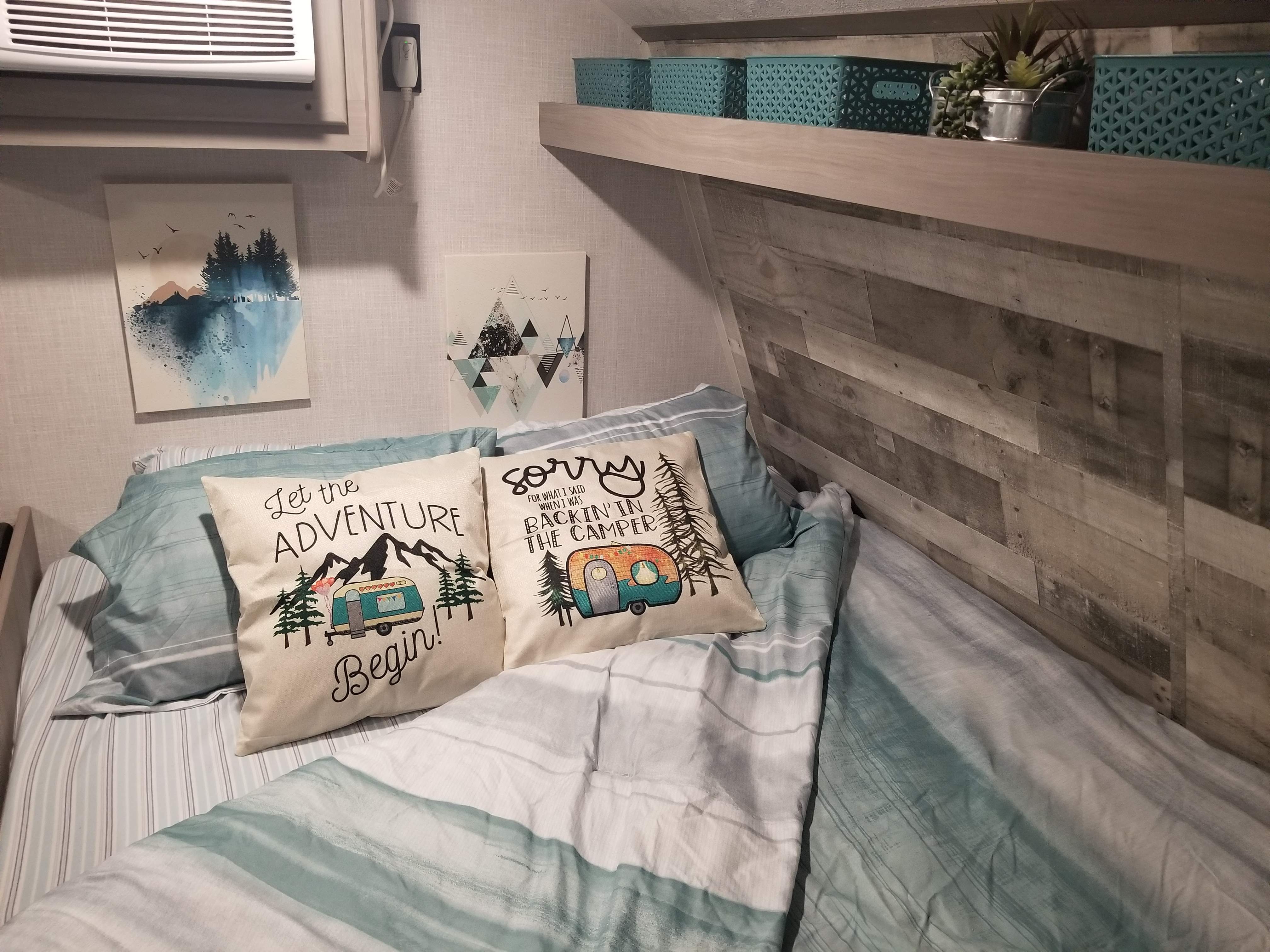 Inside a stylish rv rental: a cozy bed with camping-themed pillows, wood paneling, & teal storage. Ready for adventure!. Coleman Lantern 17B 2023