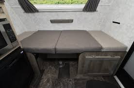 Inside this RV rental: A compact dinette with gray cushions converts to a cozy bed. Microwave and small fridge are on the left.. Prolite 12 V 2019