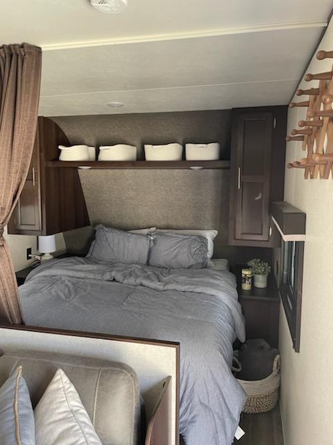 Cozy rv rental bedroom with a comfortable bed, gray bedding, overhead bins, and dark wood cabinetry. Perfect for travel.. Jayco Jay Flight SLX 2019