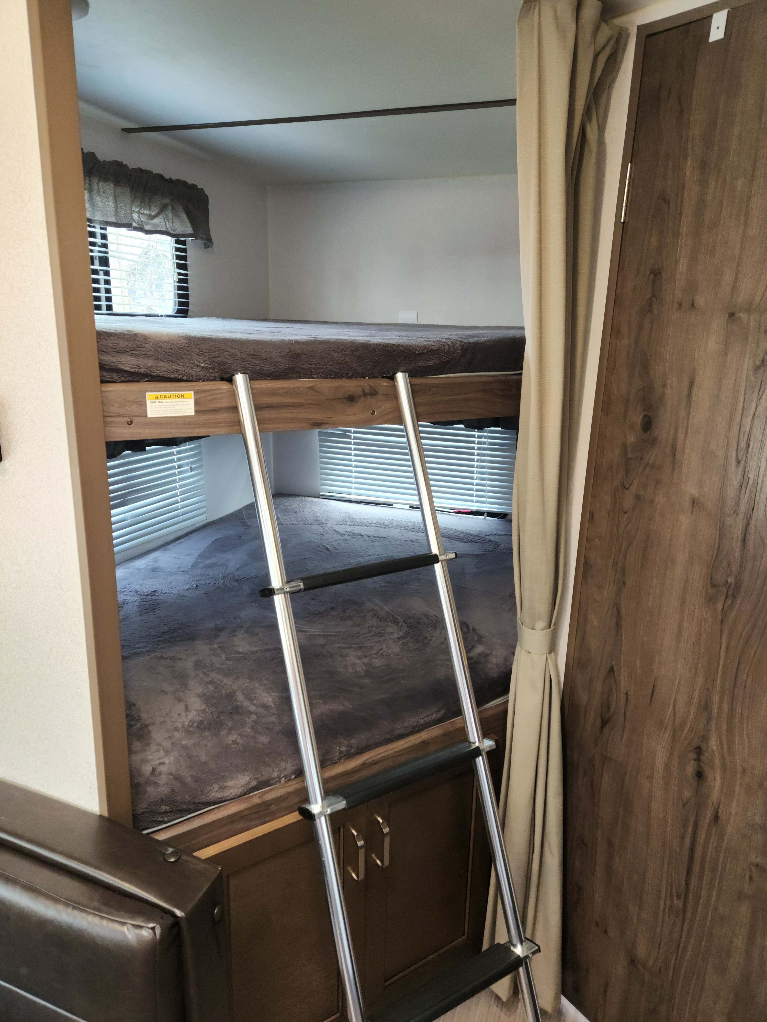 An RV rental showing bunk beds with a ladder for access. A '300 lbs. capacity' warning is visible, along with windows and curtains.. Keystone RV Passport Ultra Lite 2019
