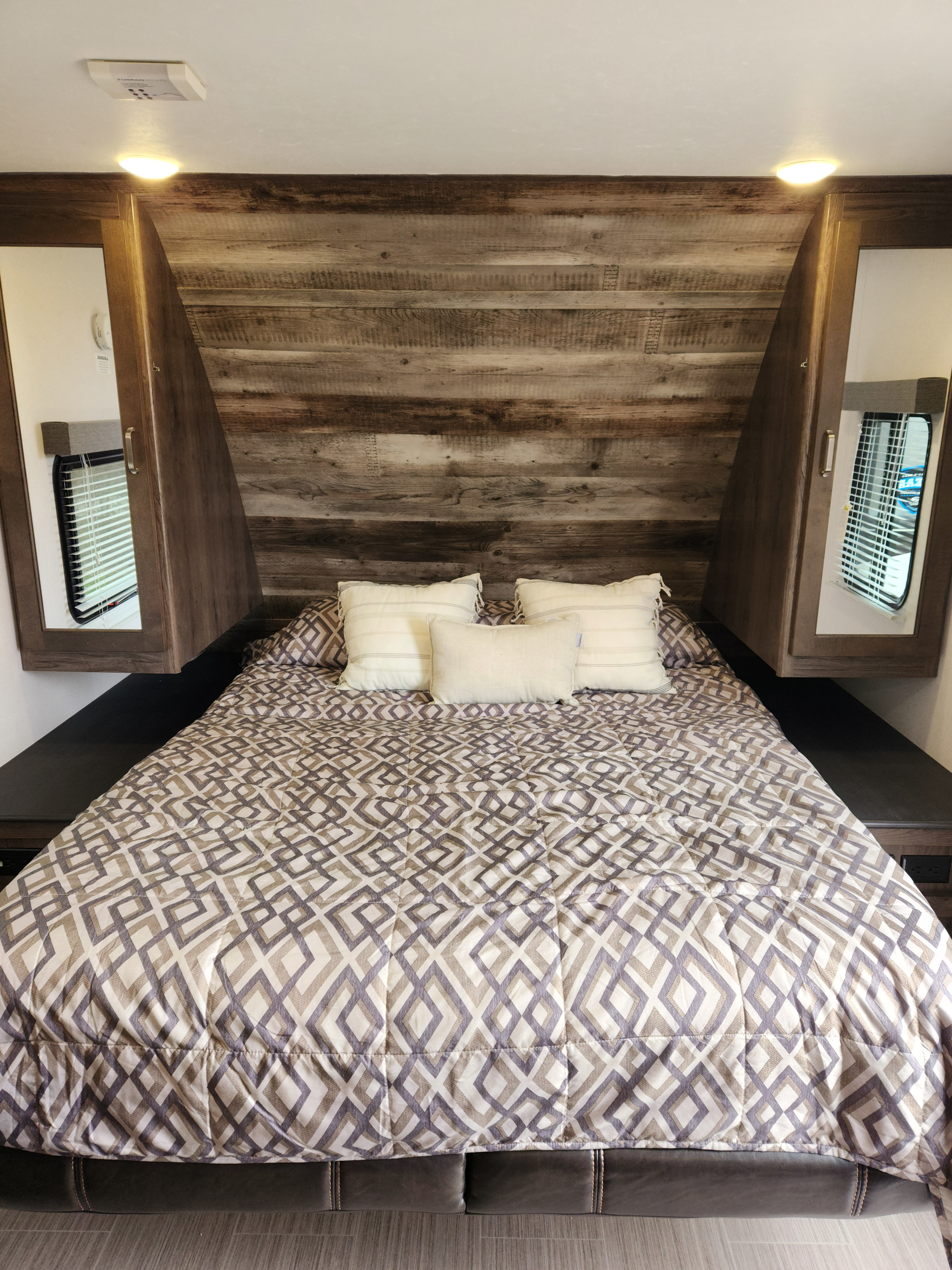 Cozy RV rental bedroom featuring a comfortable bed with a patterned comforter, wood headboard, and mirrored cabinets.. Keystone RV Passport Ultra Lite 2019