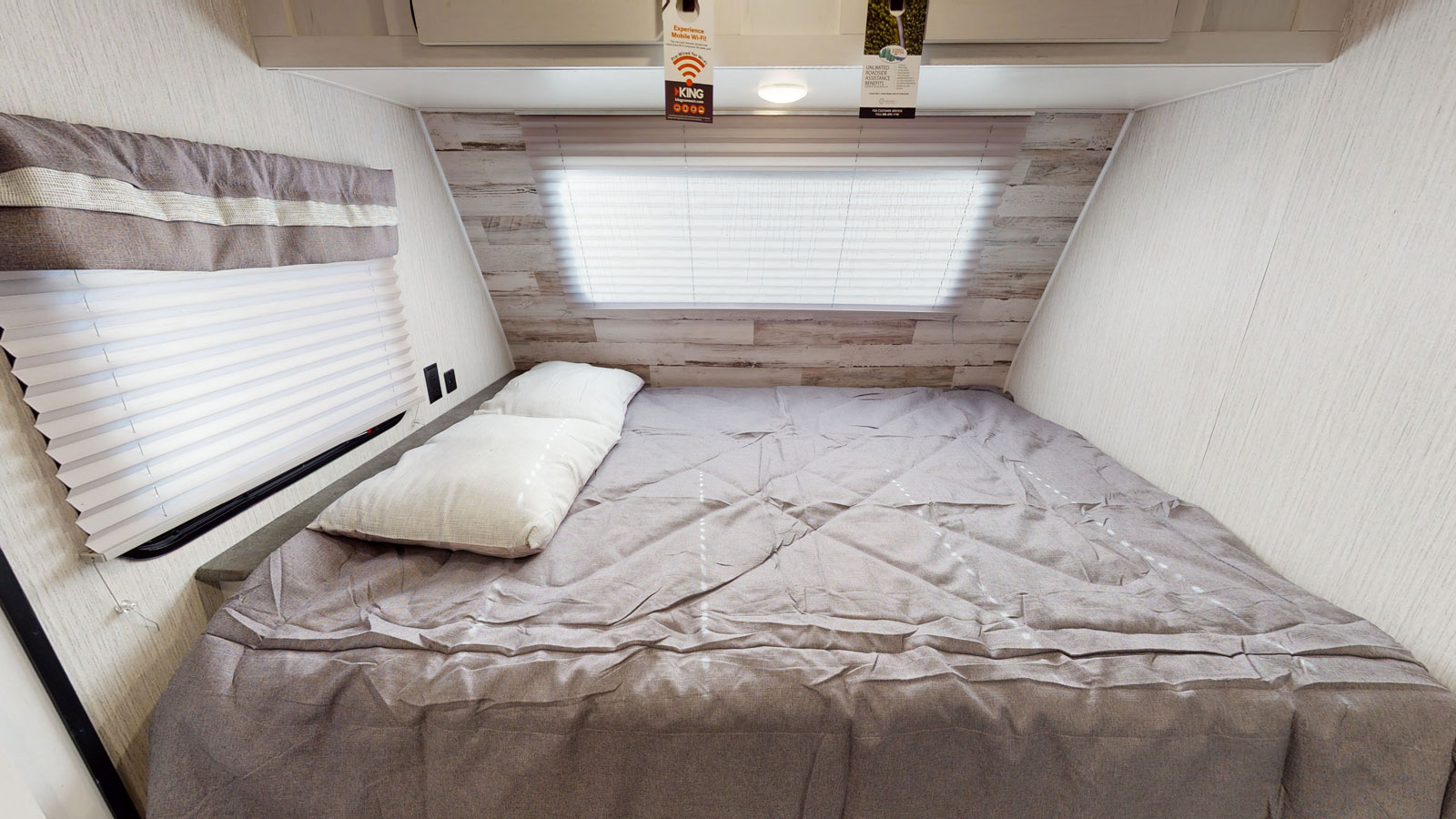 RV rental bedroom with a bed featuring gray bedding and white pillows, a window with blinds, and light wood accent wall.. Palomino Puma 18SSX 2021