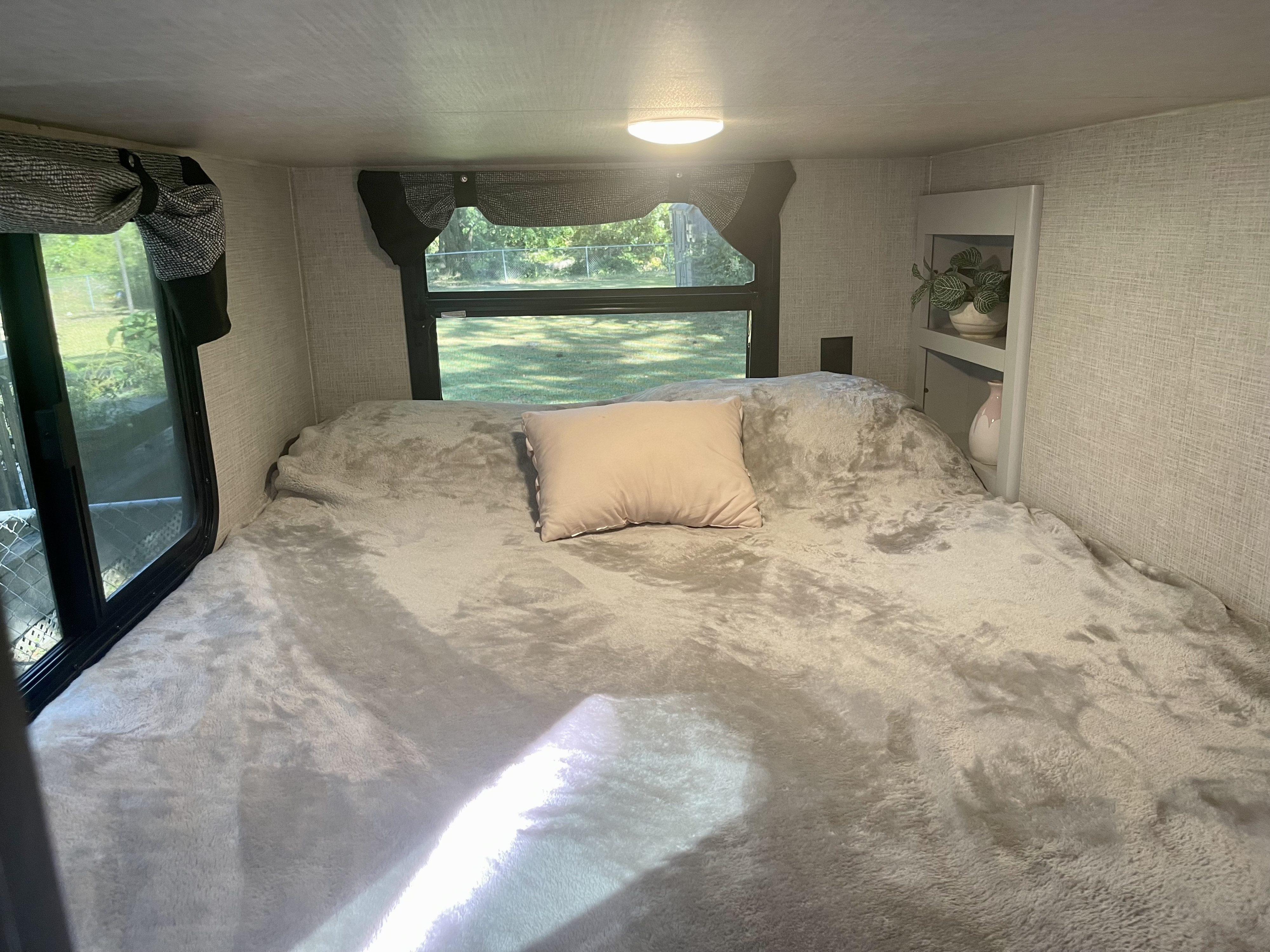 Inviting RV rental bedroom with a large, plush bed, pink pillow, and sunny windows overlooking green outdoor space.. Keystone RV Bullet Premier Ultra 2020