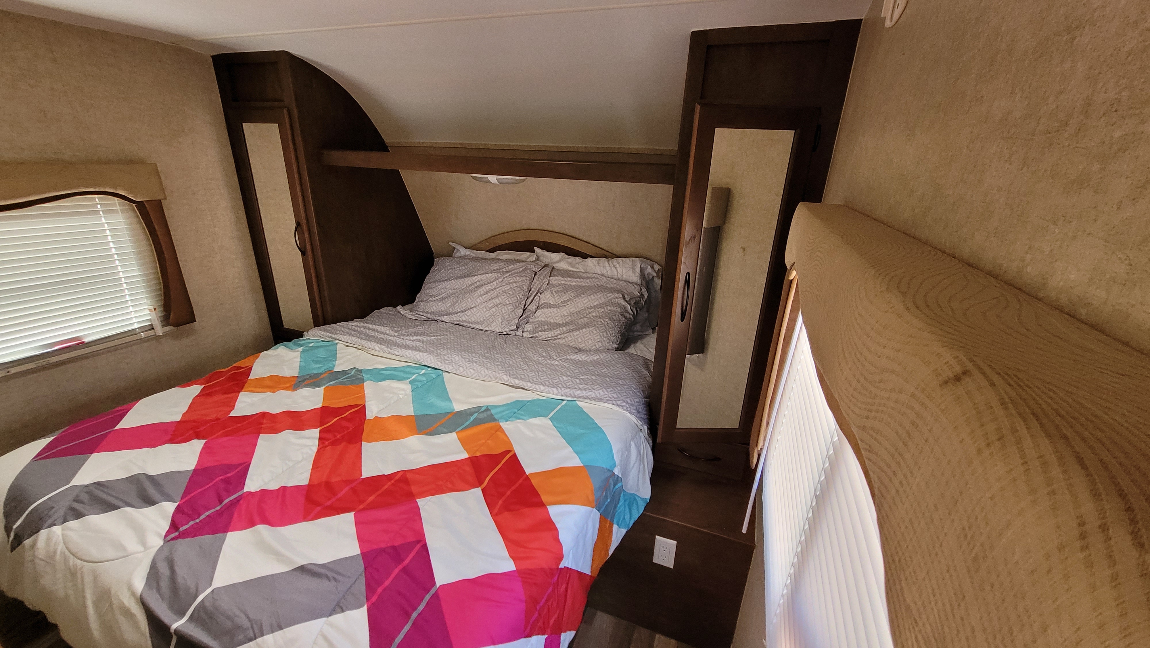 RV rental bedroom featuring a colorful comforter, patterned pillows, built-in storage, and windows with blinds.. Pacific Coachworks Tango Widelite 2015