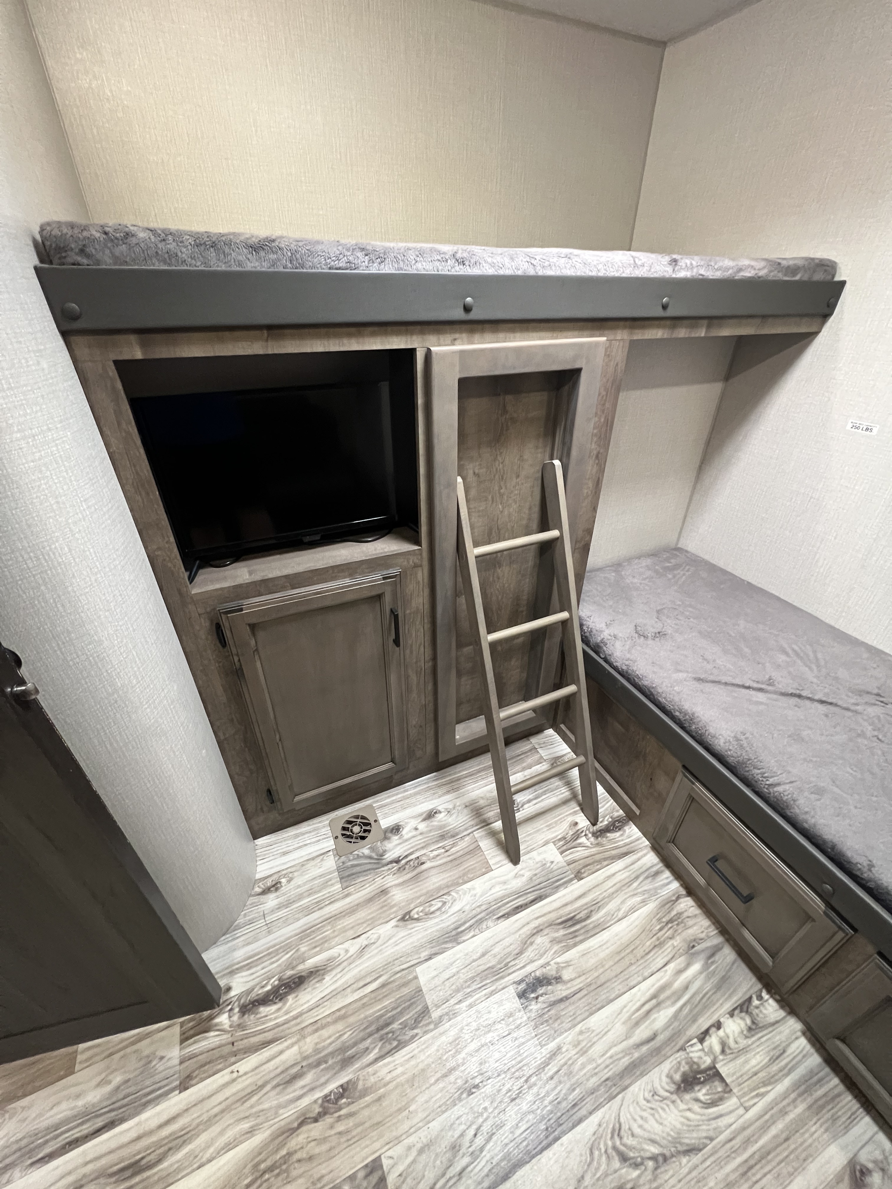 Inside an RV rental: a cozy bunk bed area with a mounted TV, ladder, and lower bed with storage drawers.. Sport Trek Sport Trek Trailer 2021