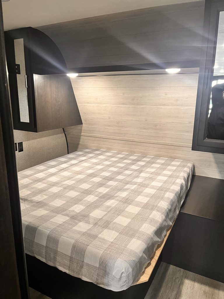 RV rental bedroom featuring a full-size bed with plaid bedding, overhead lights, and storage on both sides.. Jayco Jay Flight 2022