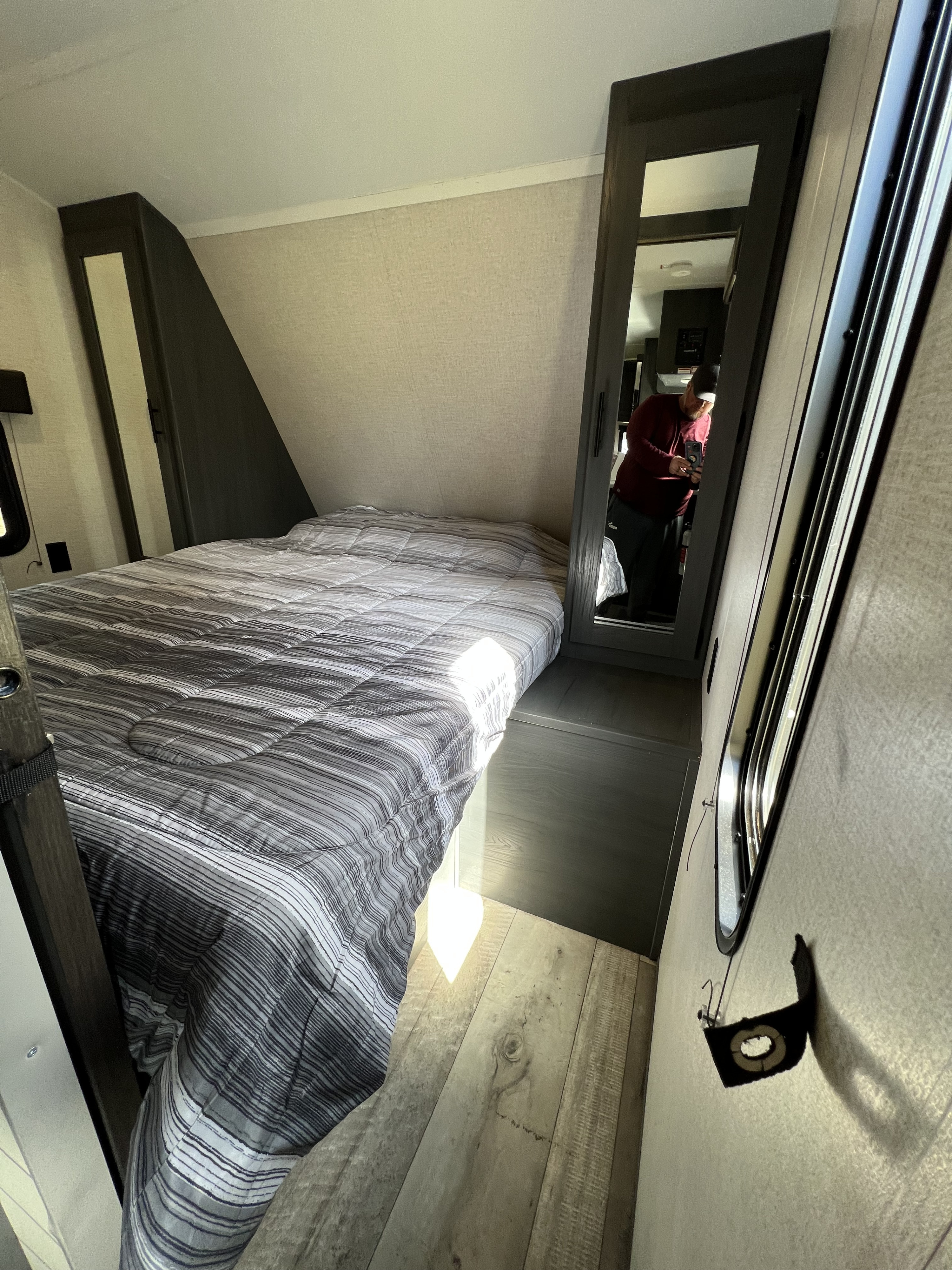 Compact RV rental bedroom featuring a striped bed, mirrored closet, and light wood flooring, offering a cozy space.. Aspen Trail LE 2022