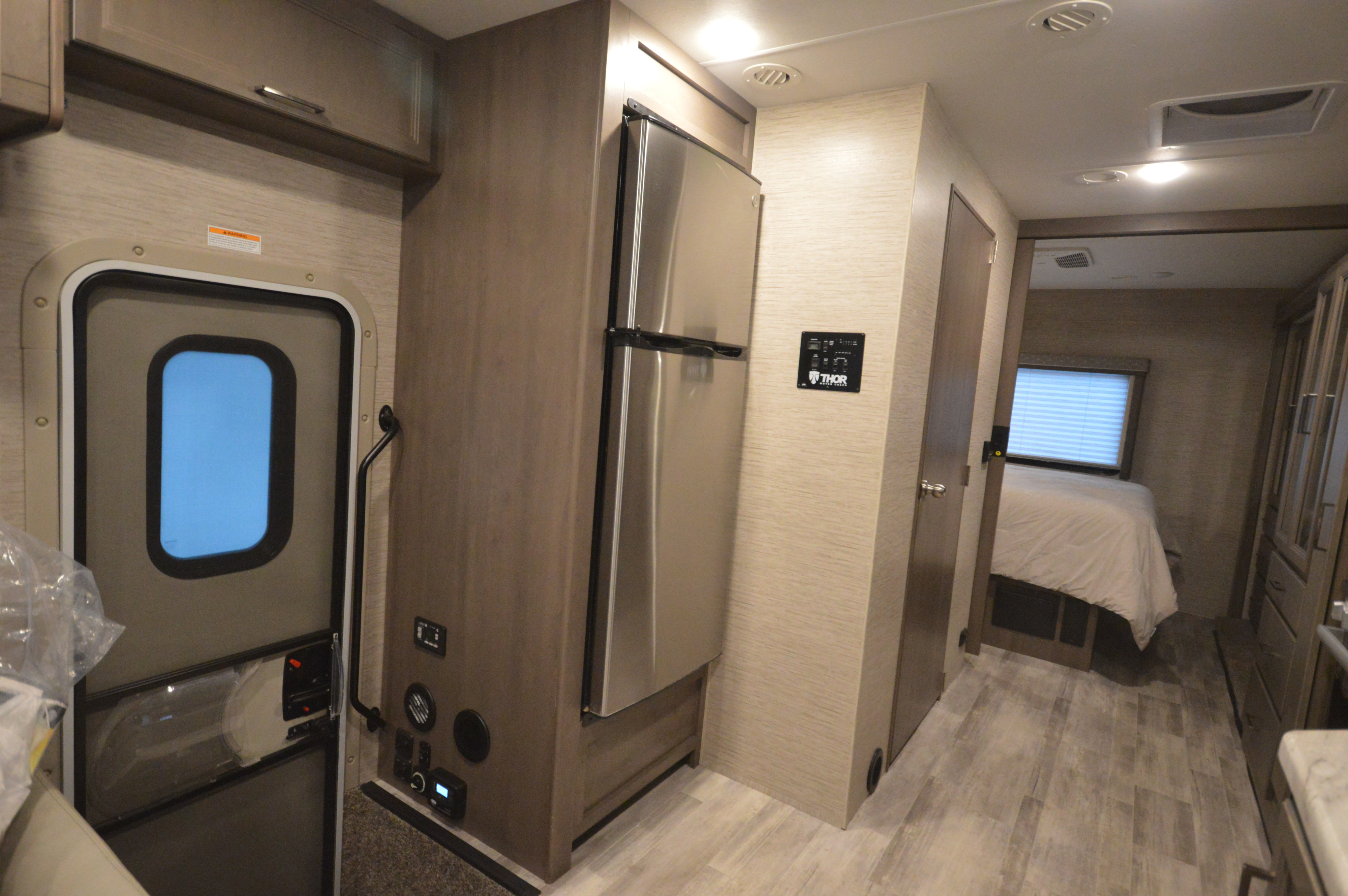 RV rental interior: A hallway view shows the entry door, stainless steel fridge, control panel, and rear bedroom.. Thor Motor Coach Freedom Traveler 2023