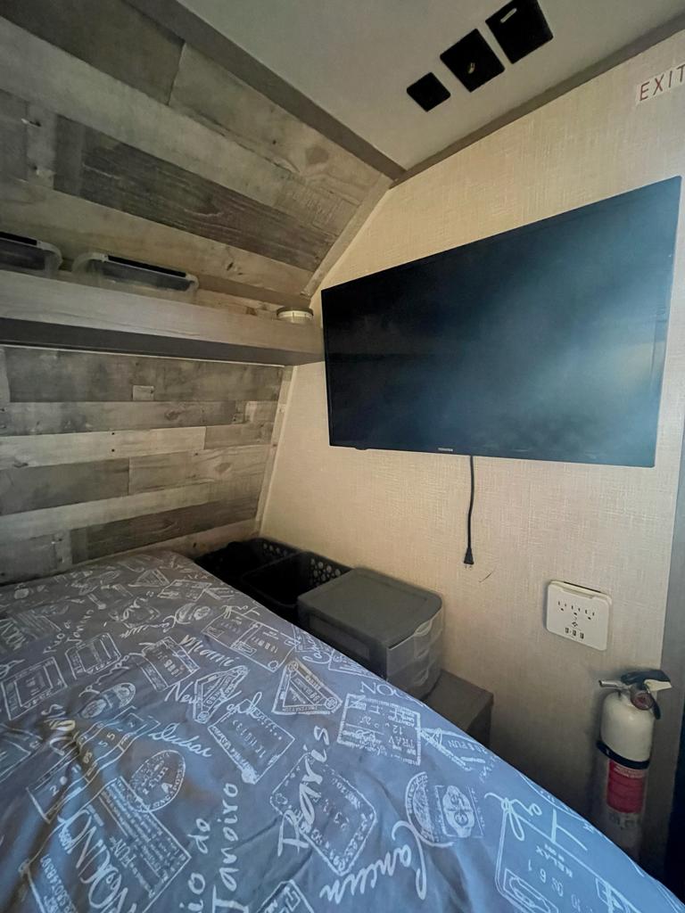 RV rental bedroom with a mounted TV, patterned bed, power outlets, and safety equipment for a comfortable stay.. Dutchmen Coleman Lantern LT 2022